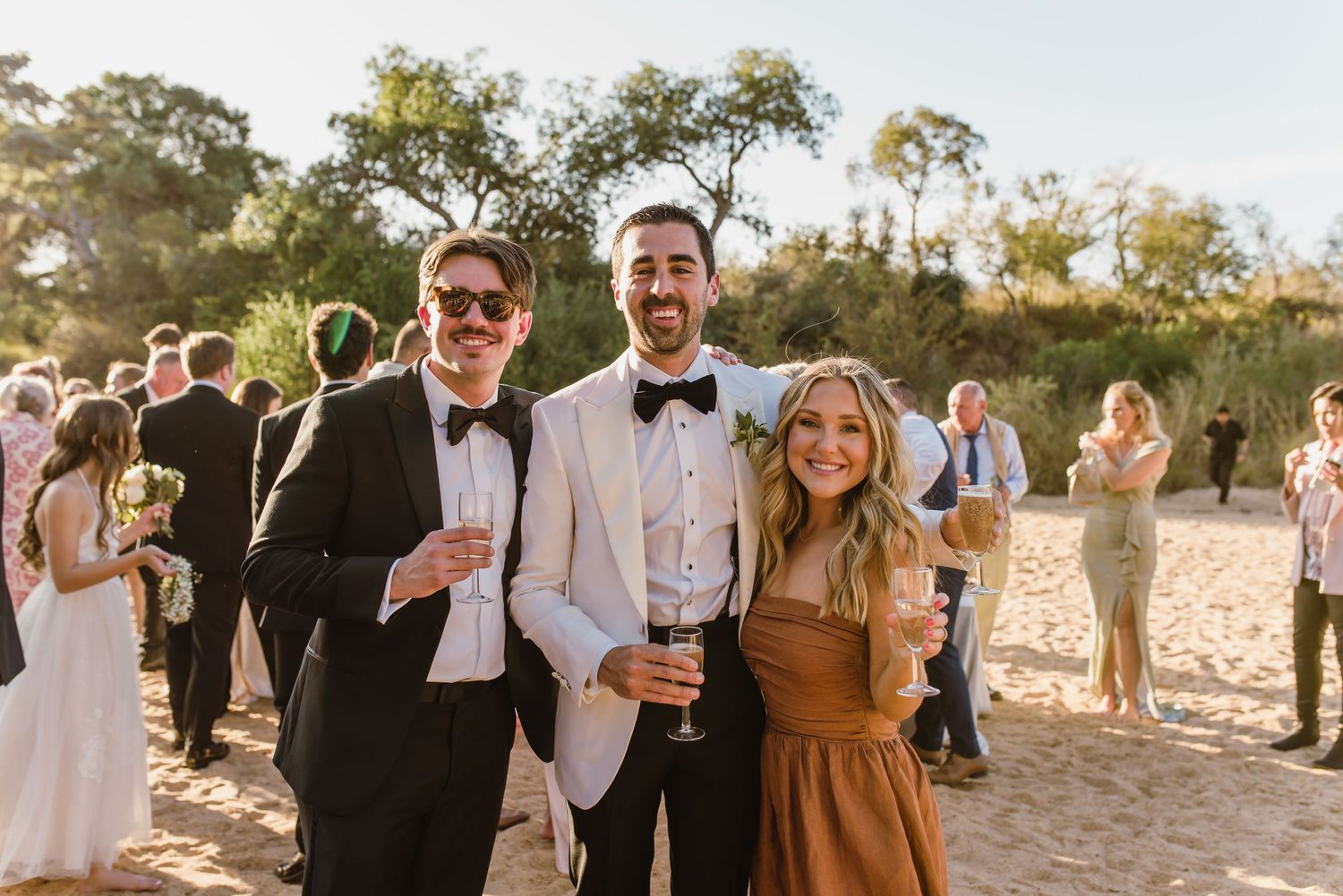 Festive wedding guests socializing and celebrating on a sandy beach during sunset.
