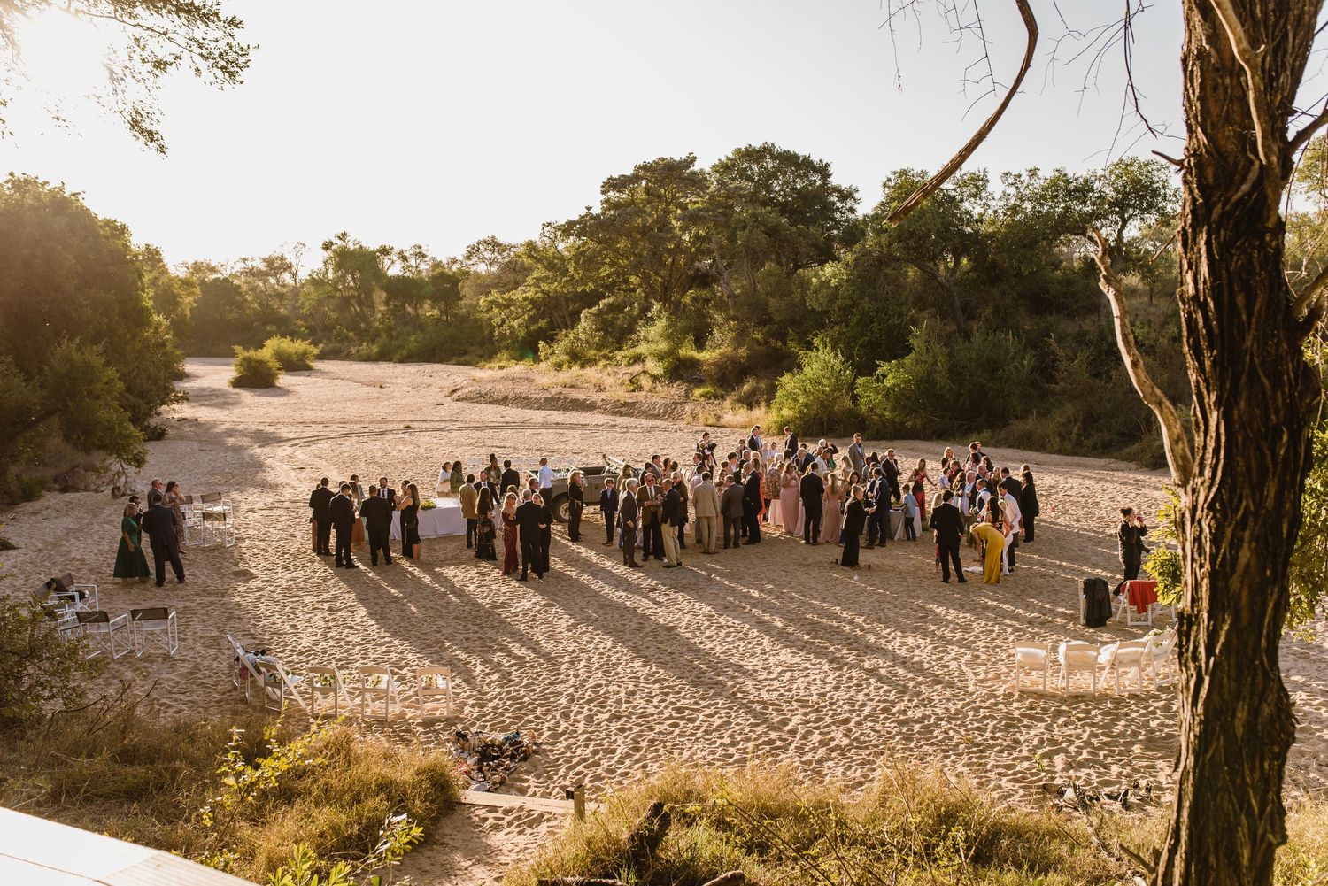 Panoramic view of beach wedding setup with guests gathering at sunset.