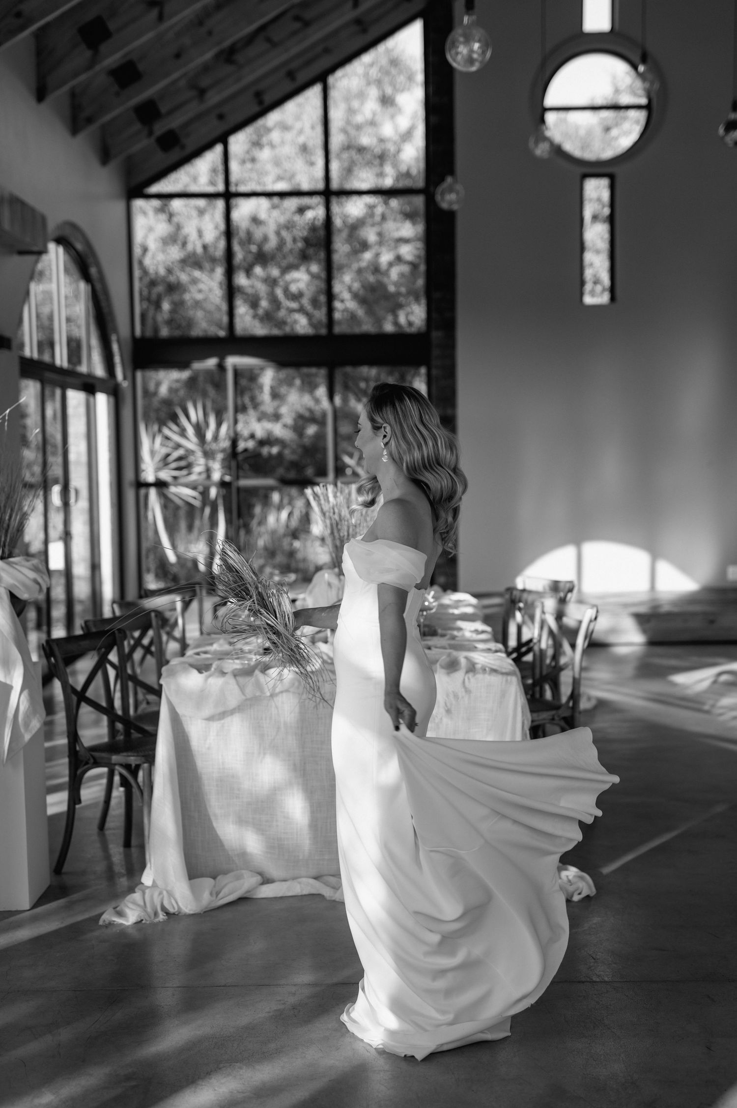 Black and white photo of a flowing wedding dress in a light-filled venue.