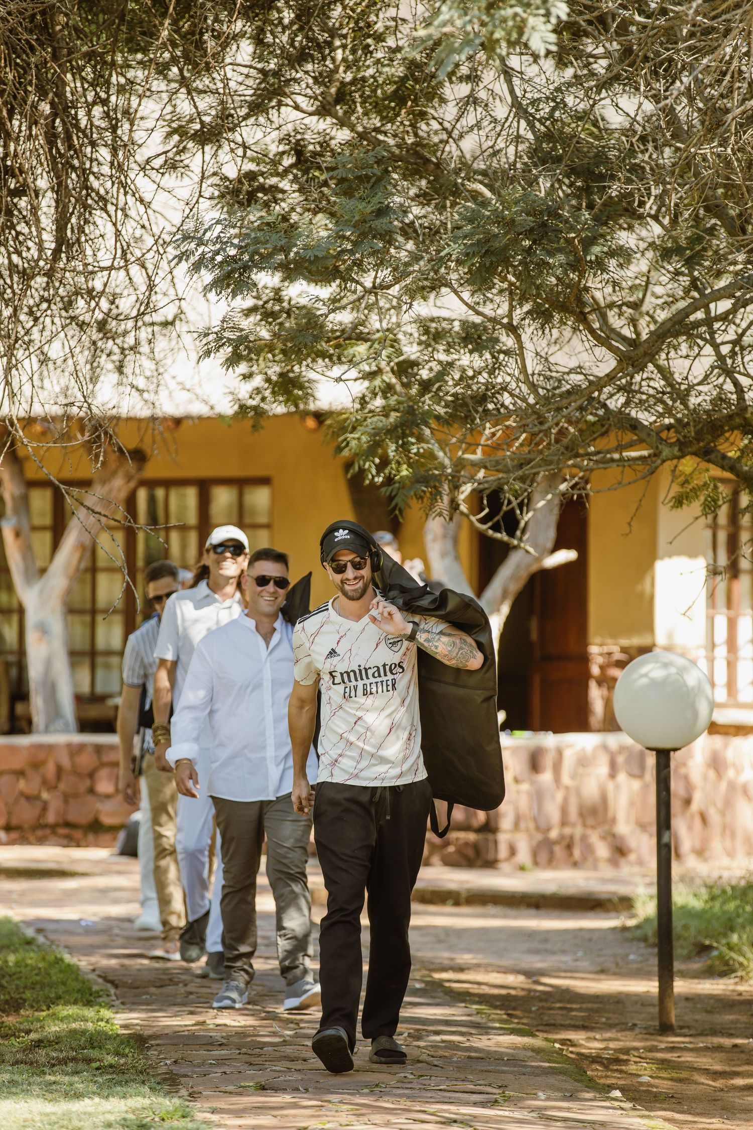 Group walking along shaded path outside yellow lodge buildings in safari setting.