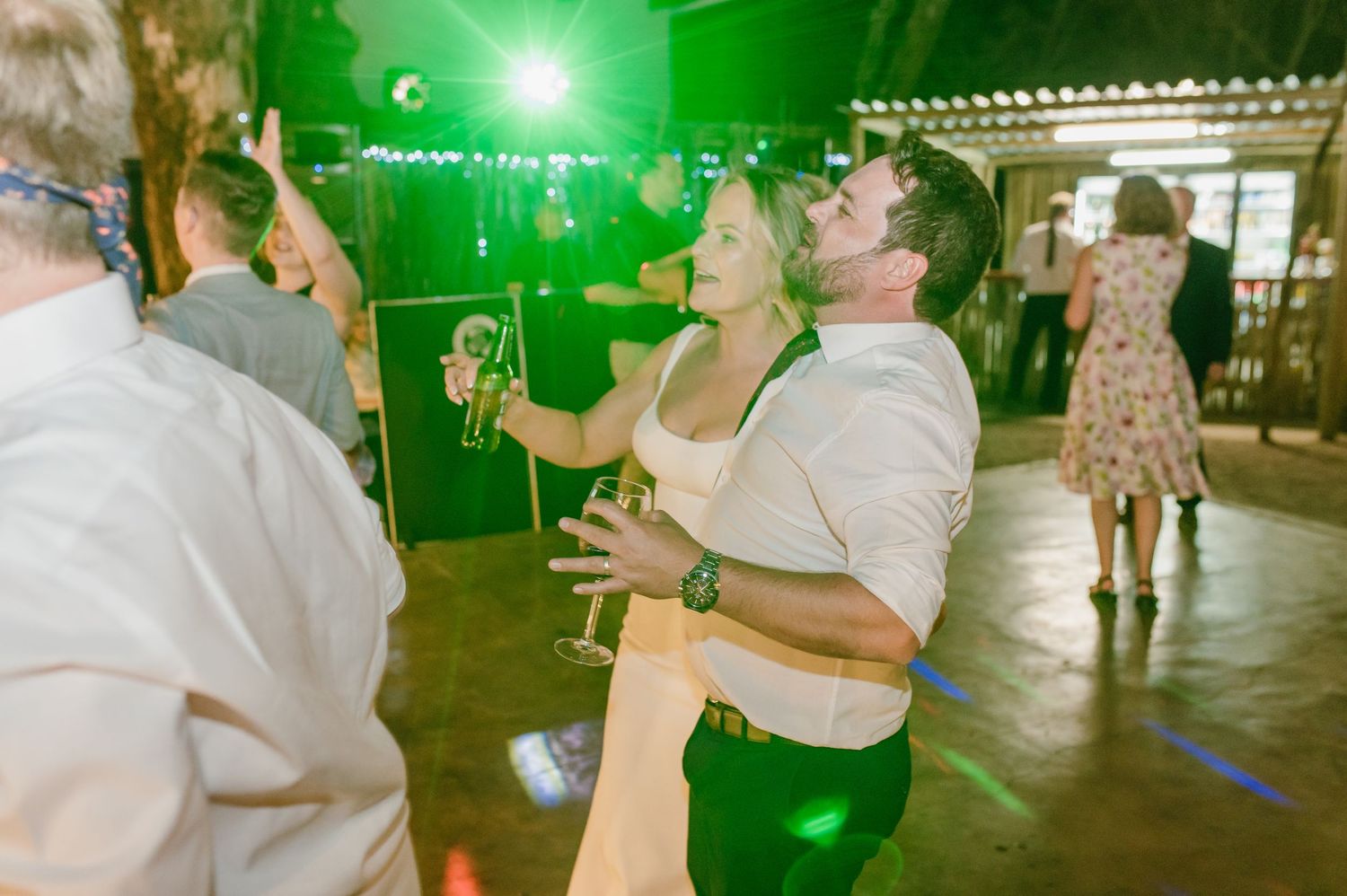 Wedding guests dancing under green party lights at outdoor evening reception.