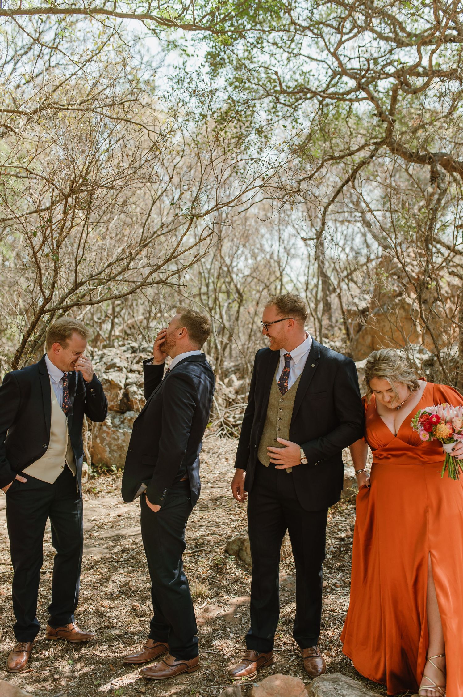 A candid moment of a wedding party laughing together in a natural outdoor setting.