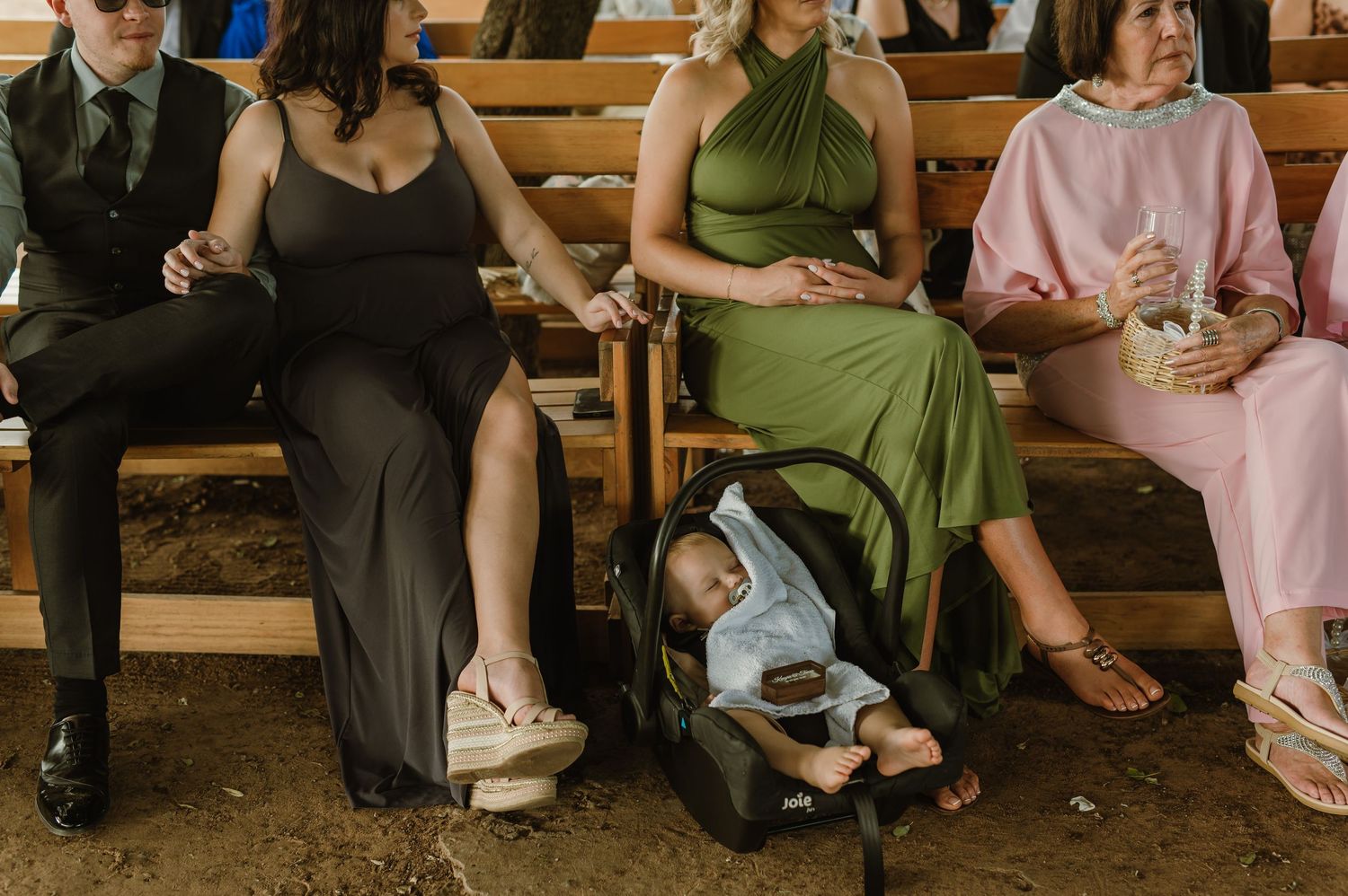 Wedding guests seated on wooden benches during an outdoor ceremony.