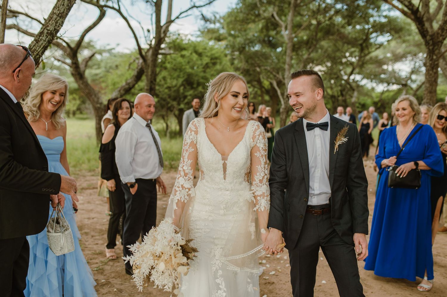 Wedding guests gather under shady trees for an outdoor celebration.