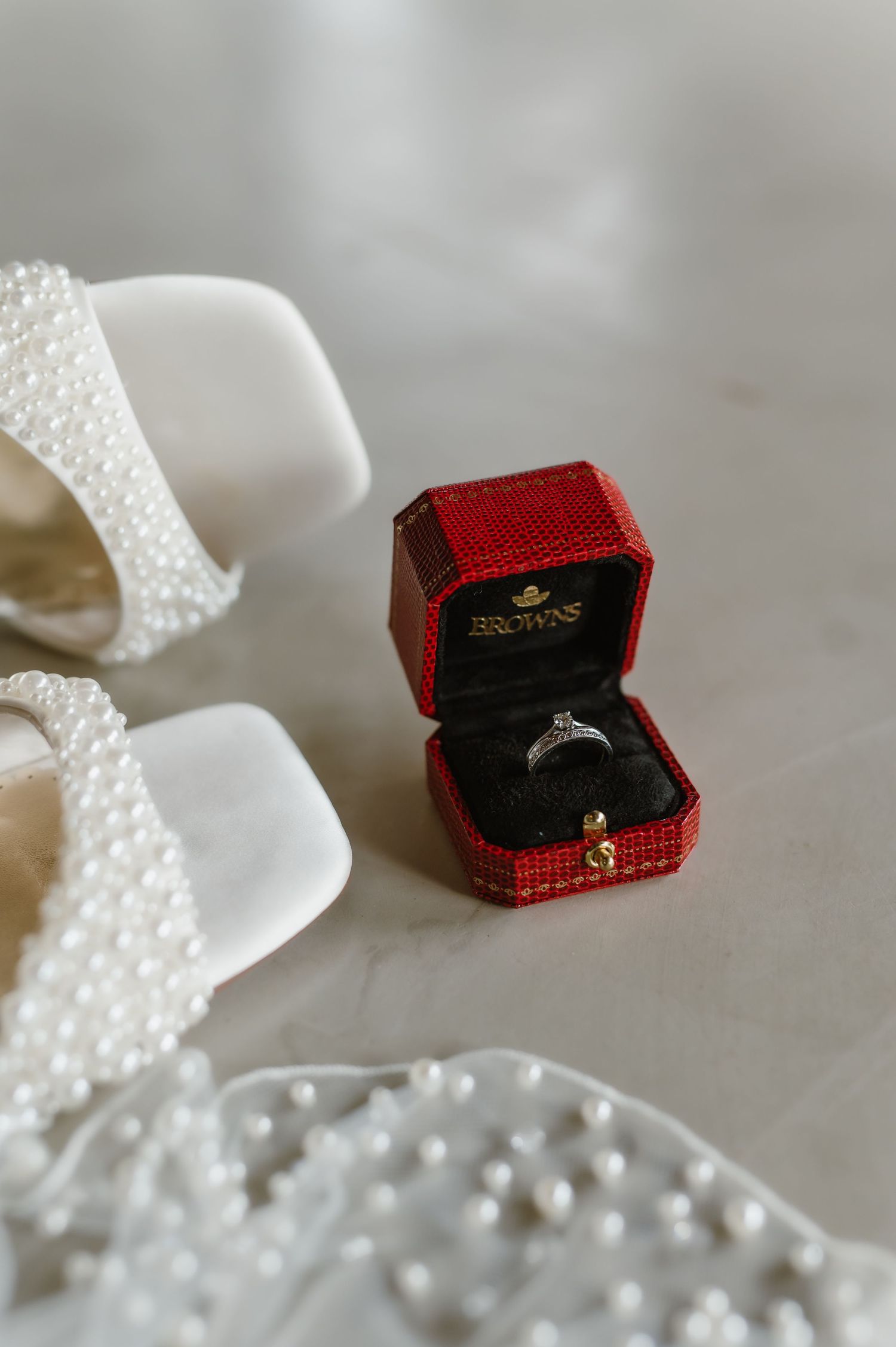 Diamond engagement ring in red velvet box with pearl accessories.