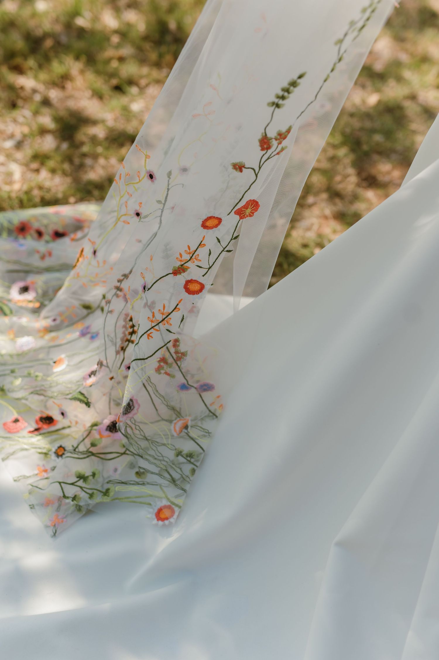 Delicate floral embroidery detail on flowing white wedding dress fabric.