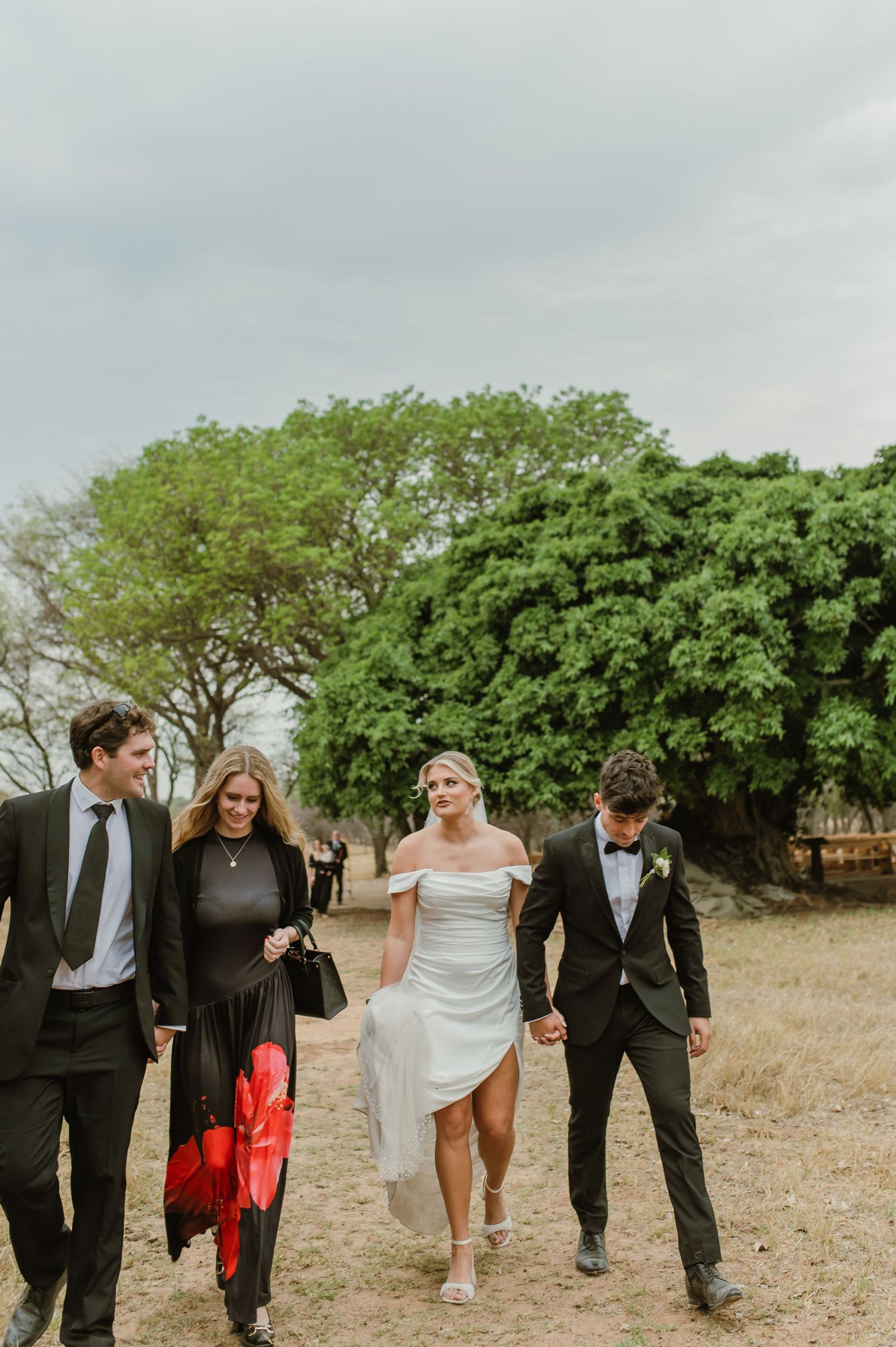 Wedding party walks along outdoor path surrounded by lush greenery.