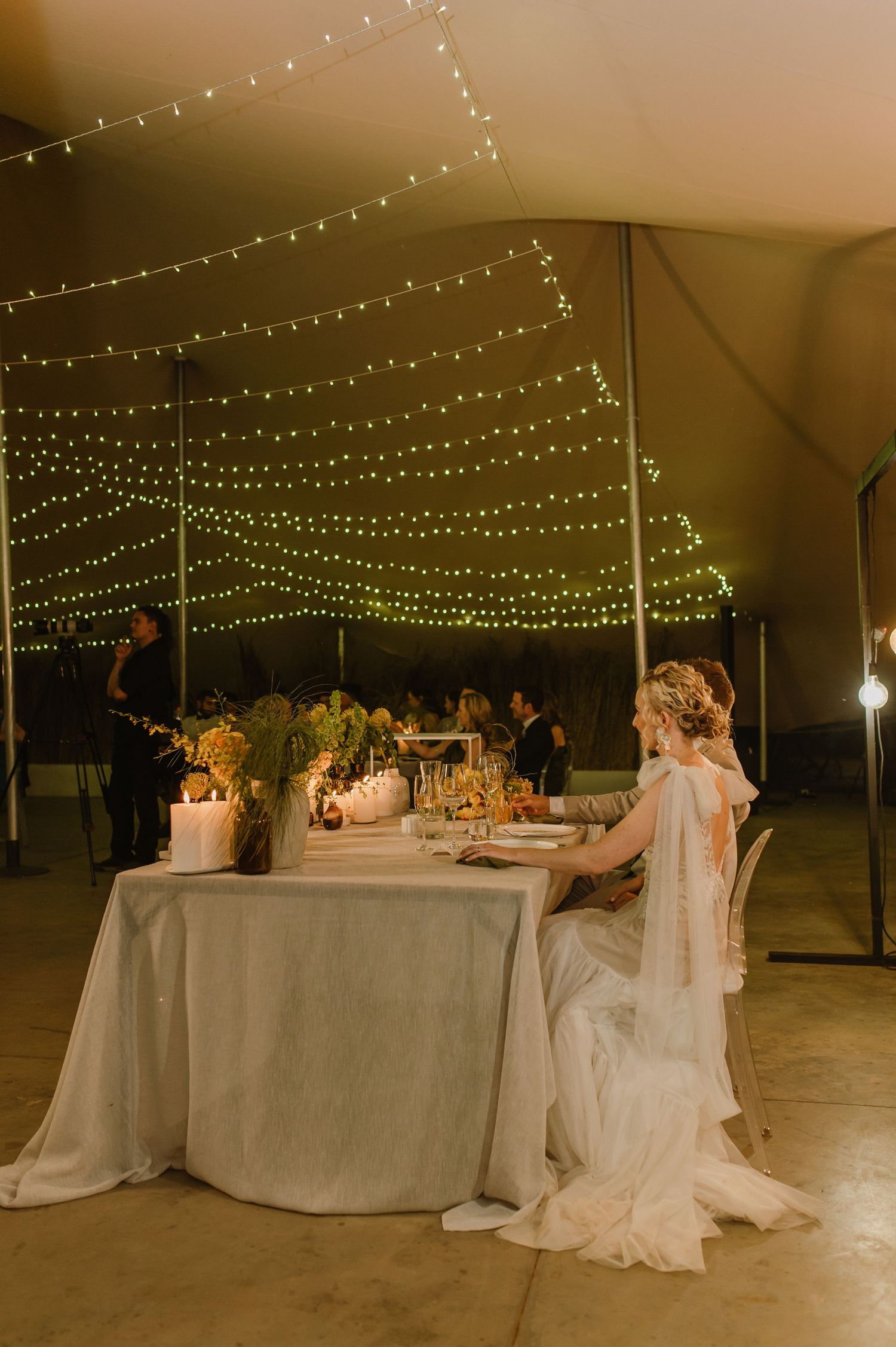 Wedding reception tent decorated with string lights and elegant white tablescapes.