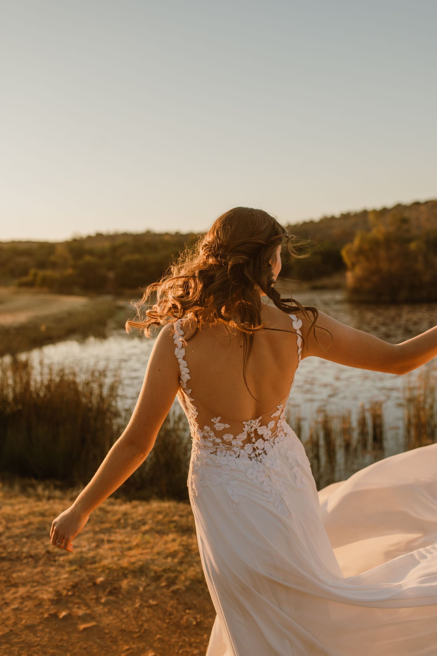 A bride in a flowing white dress twirls at sunset against a natural landscape backdrop.