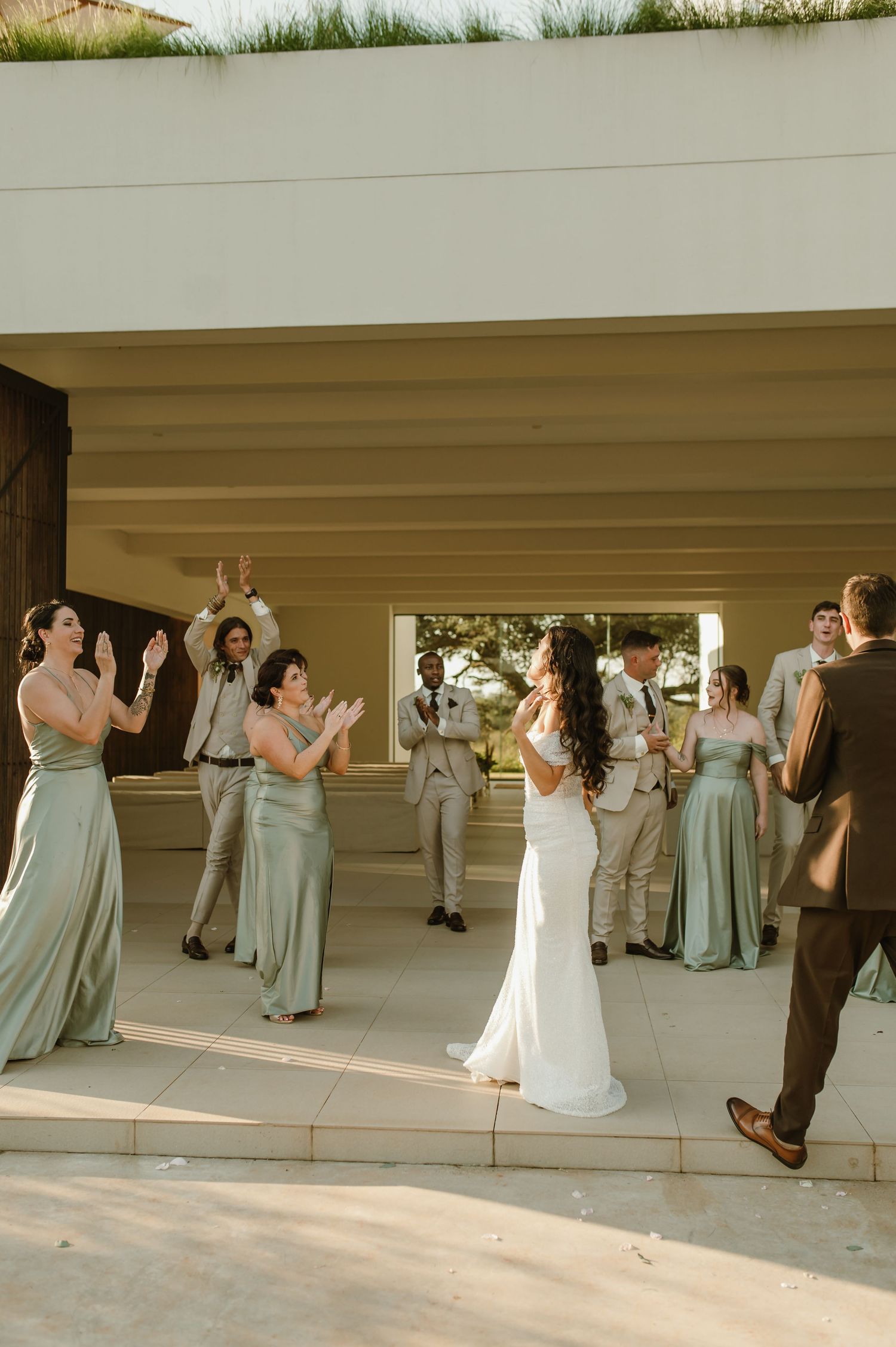 Bridal party celebrates in modern architectural setting with sage green and neutral attire.