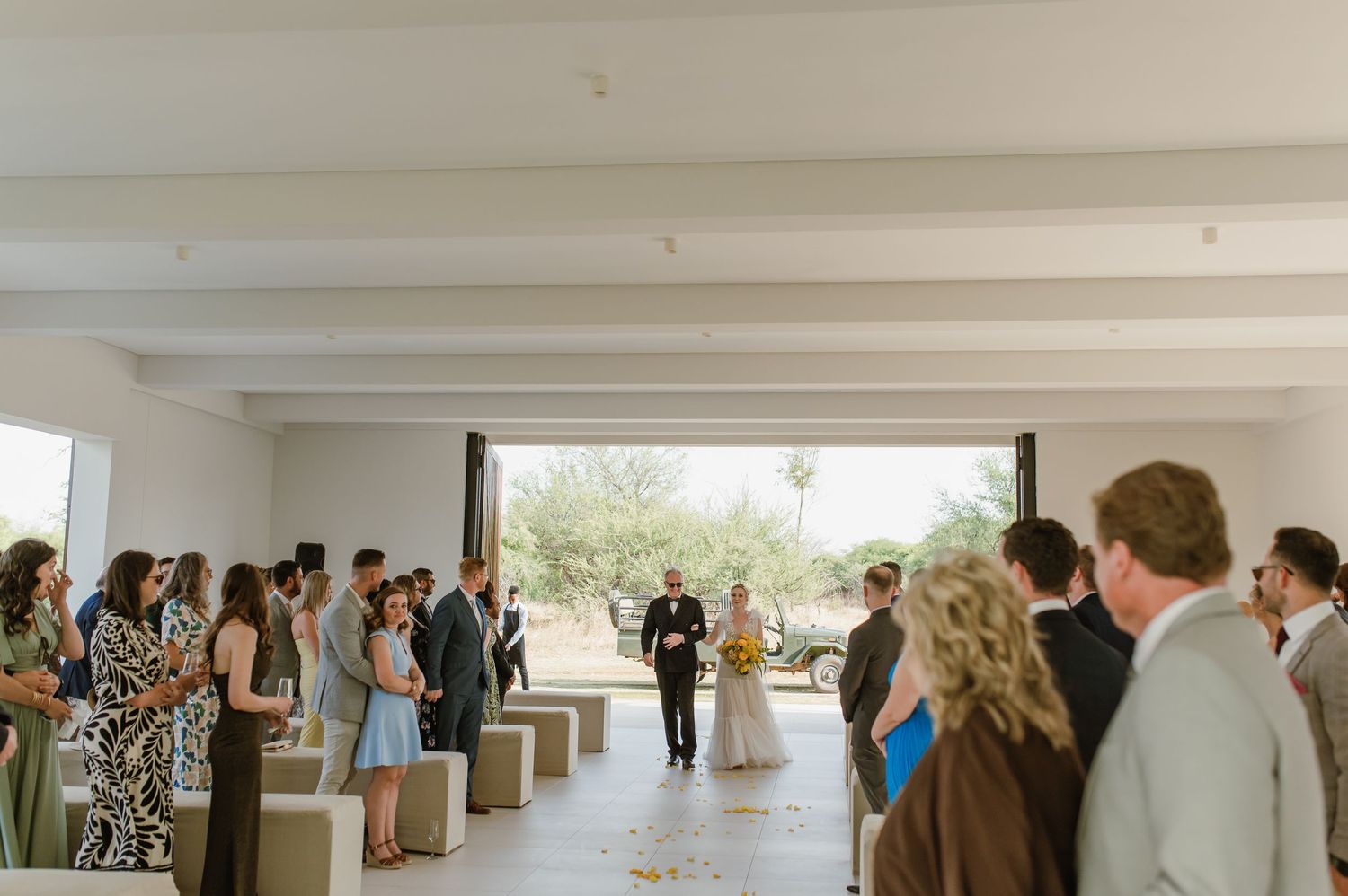 Wedding guests gather in a bright modern space with desert views through large windows.