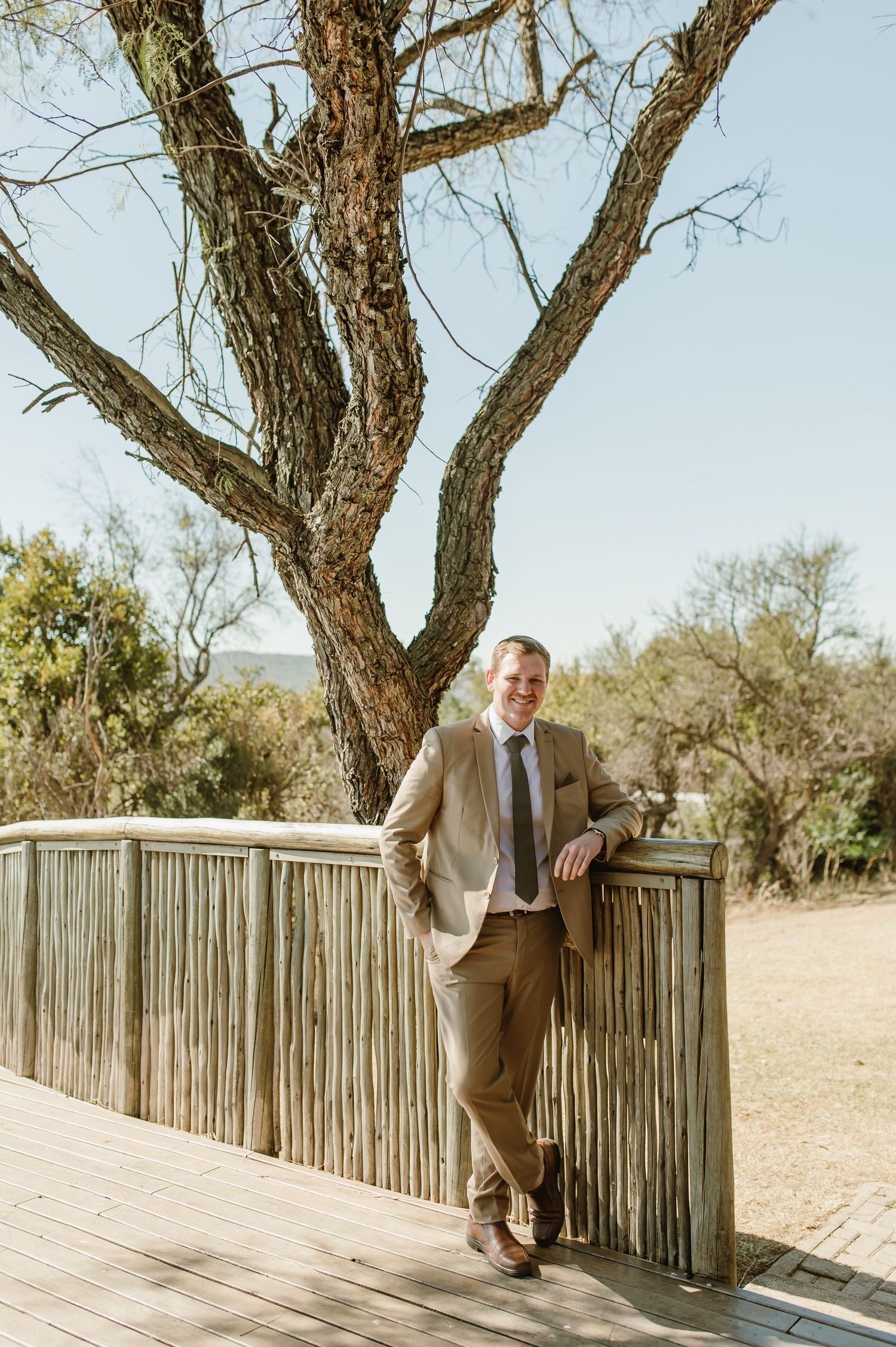 Person poses along wooden railing with African savanna landscape in background.