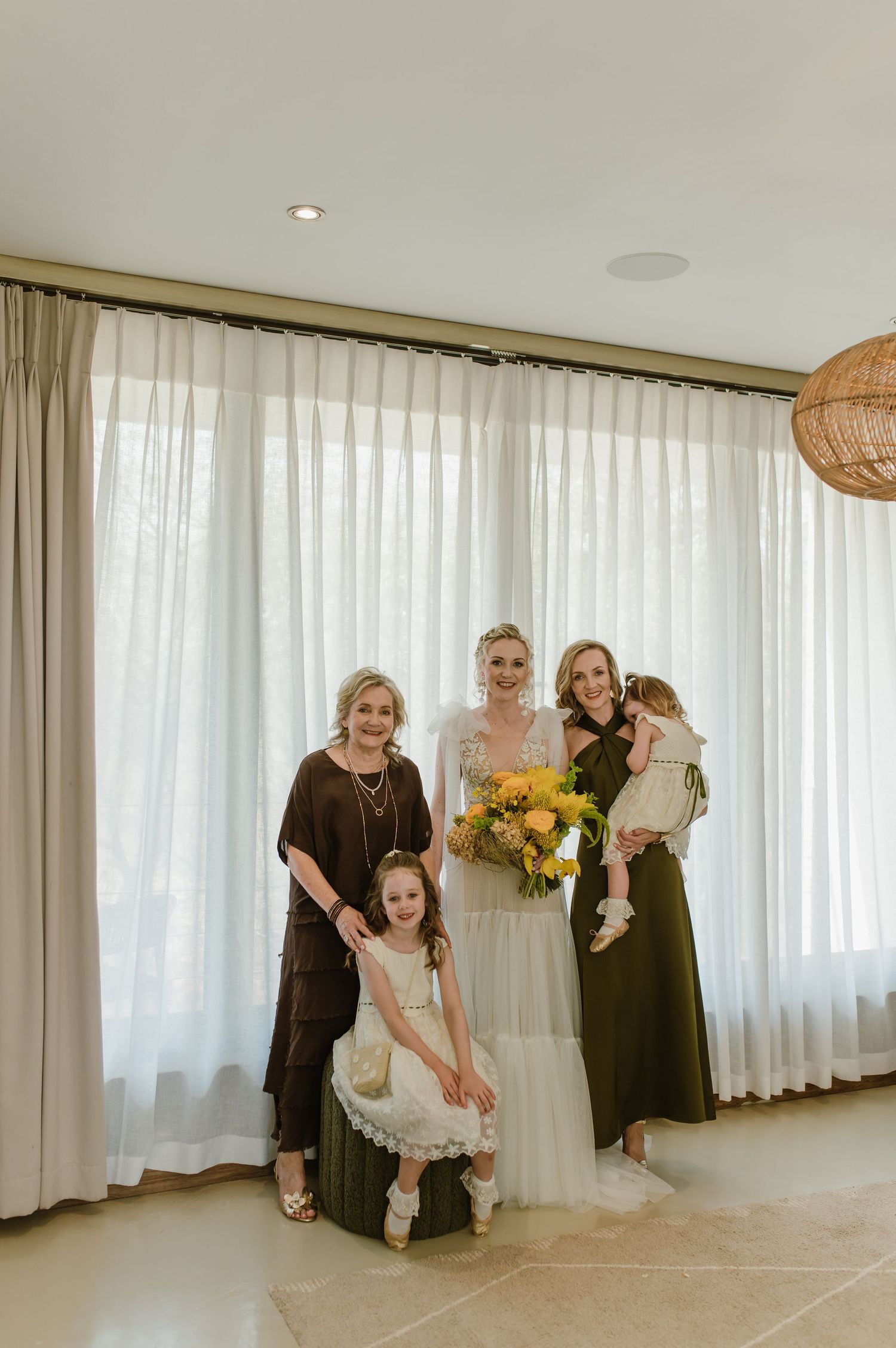 Wedding party sharing joyful moments in a bright room with sunflowers and white curtains.