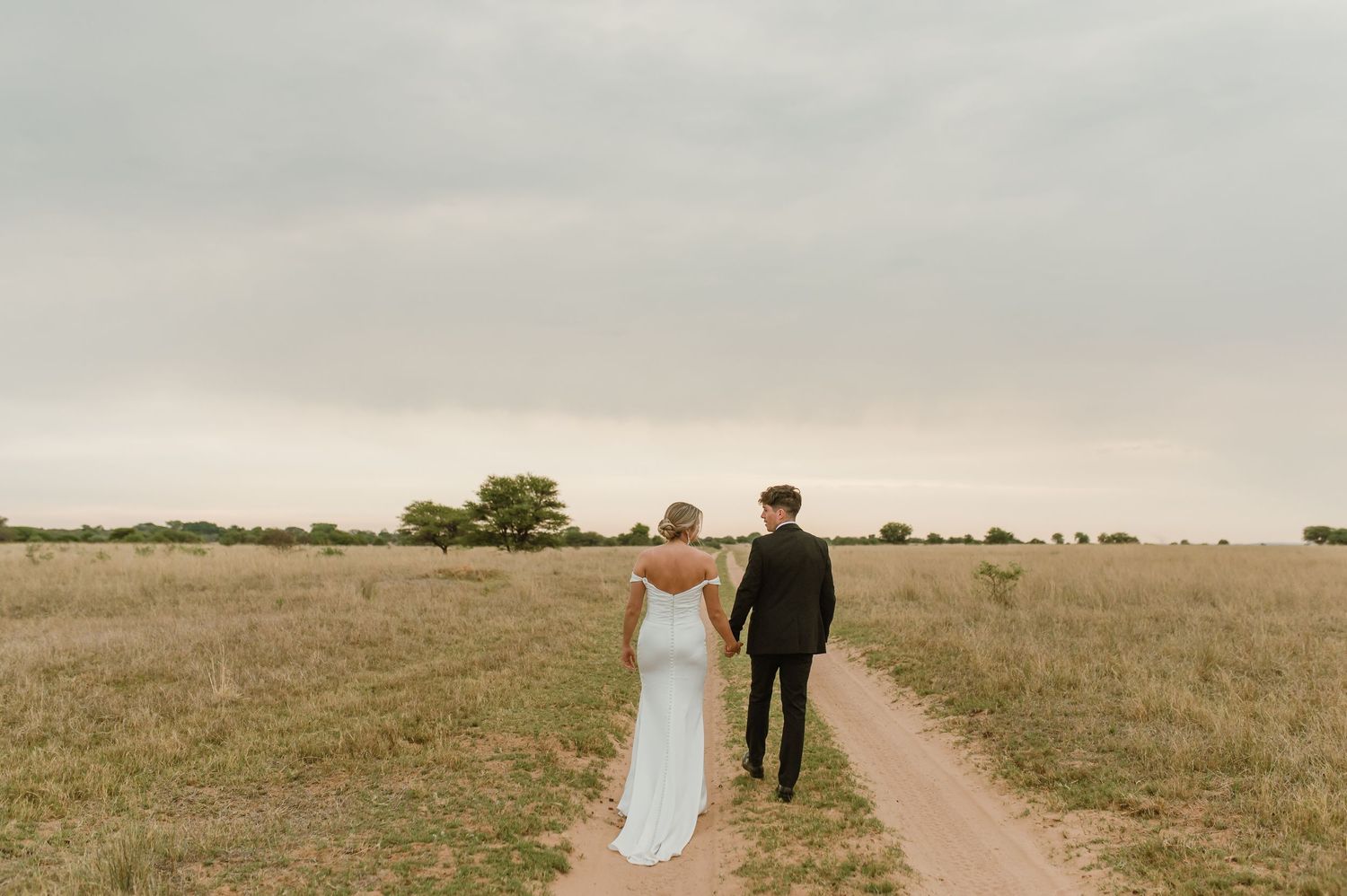 Wide landscape wedding photos showing a couple walking along a dirt path through an open field.
