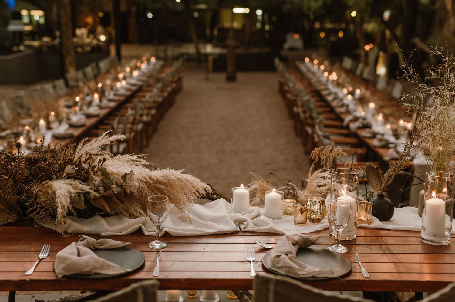Rustic outdoor reception tables decorated with elegant place settings and ambient lighting.