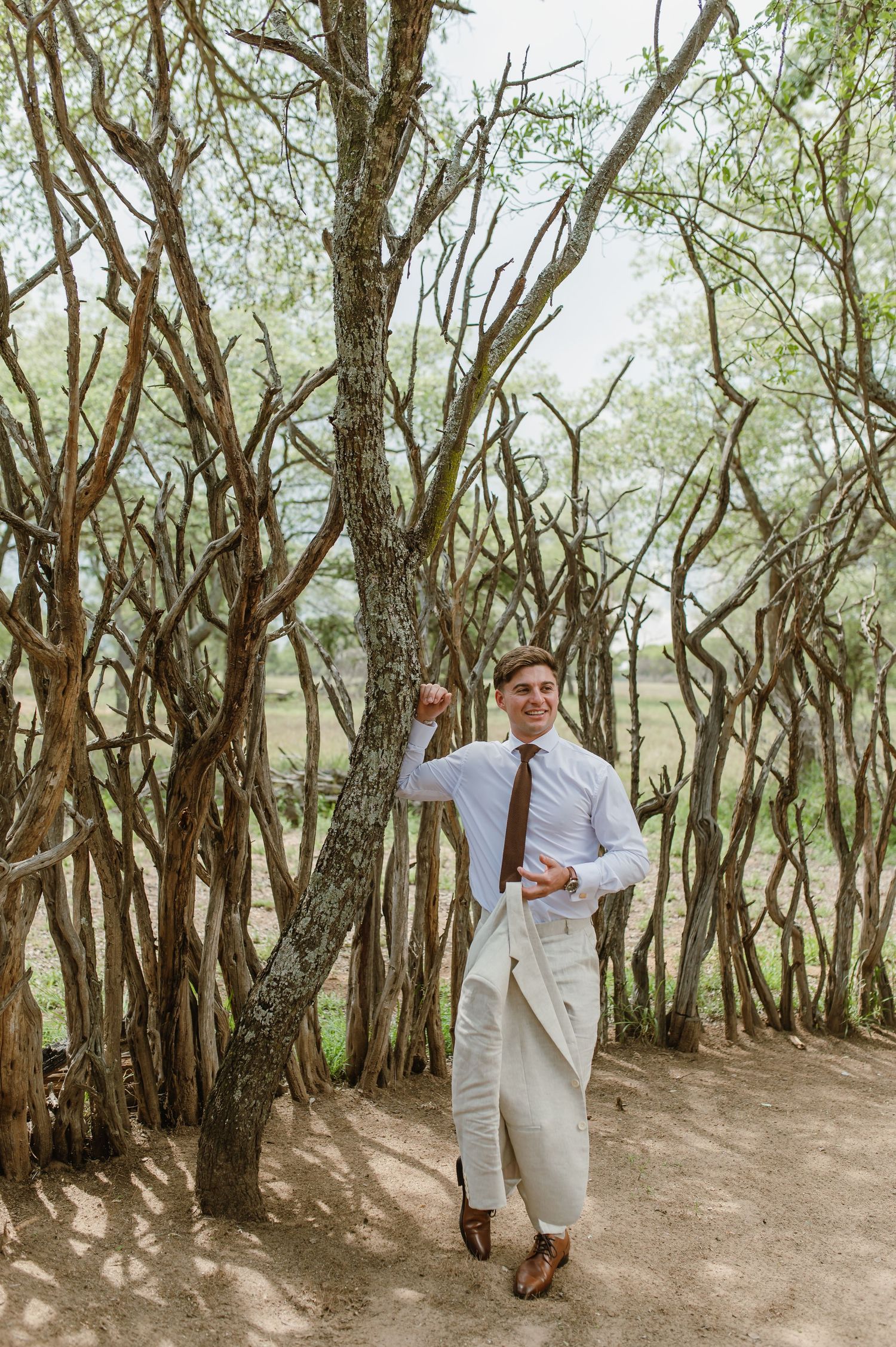 Wedding party members in light suits walk through a scenic wooded path.