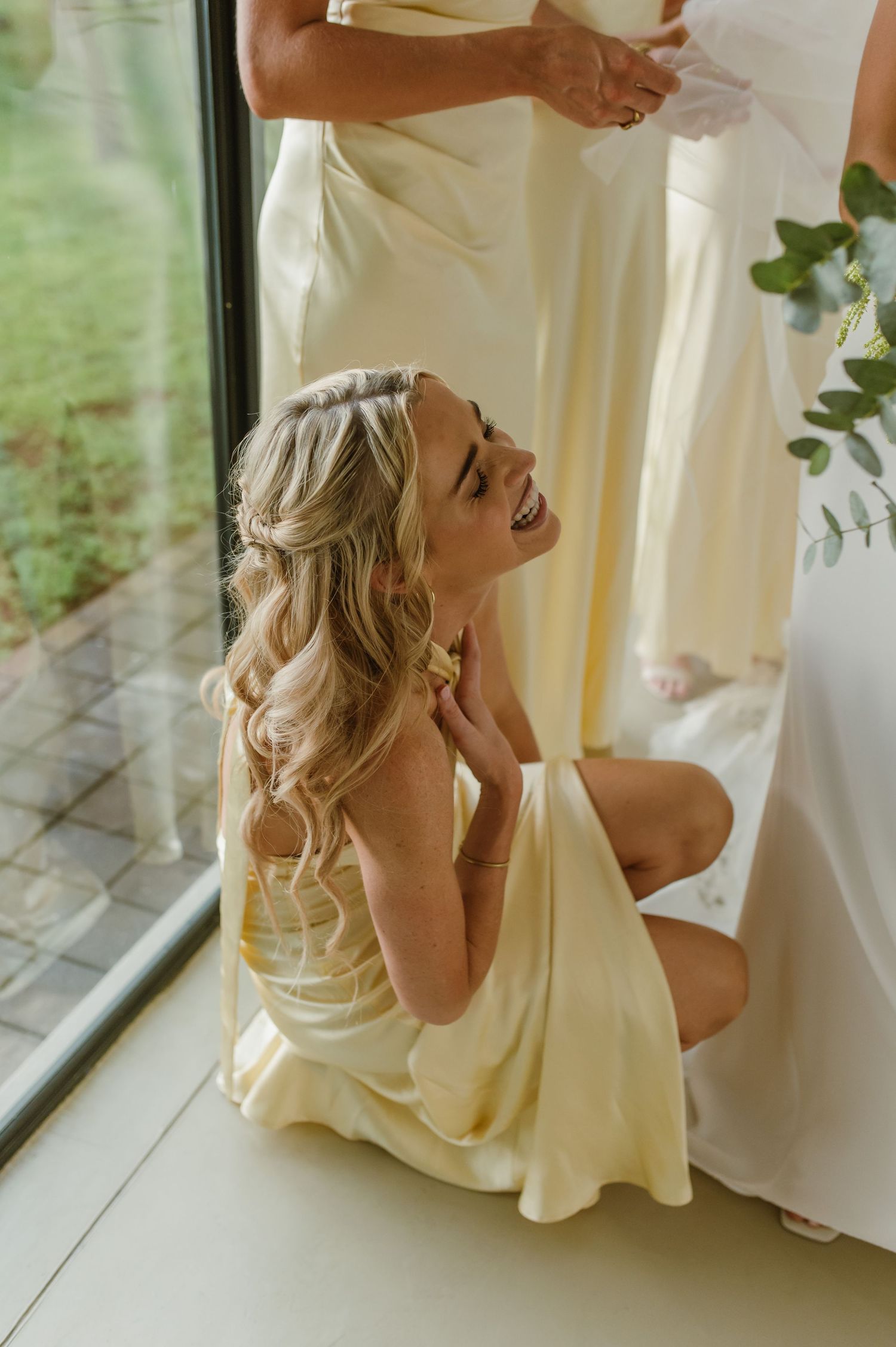 Bridesmaids in pale yellow dresses laughing together during wedding preparations.