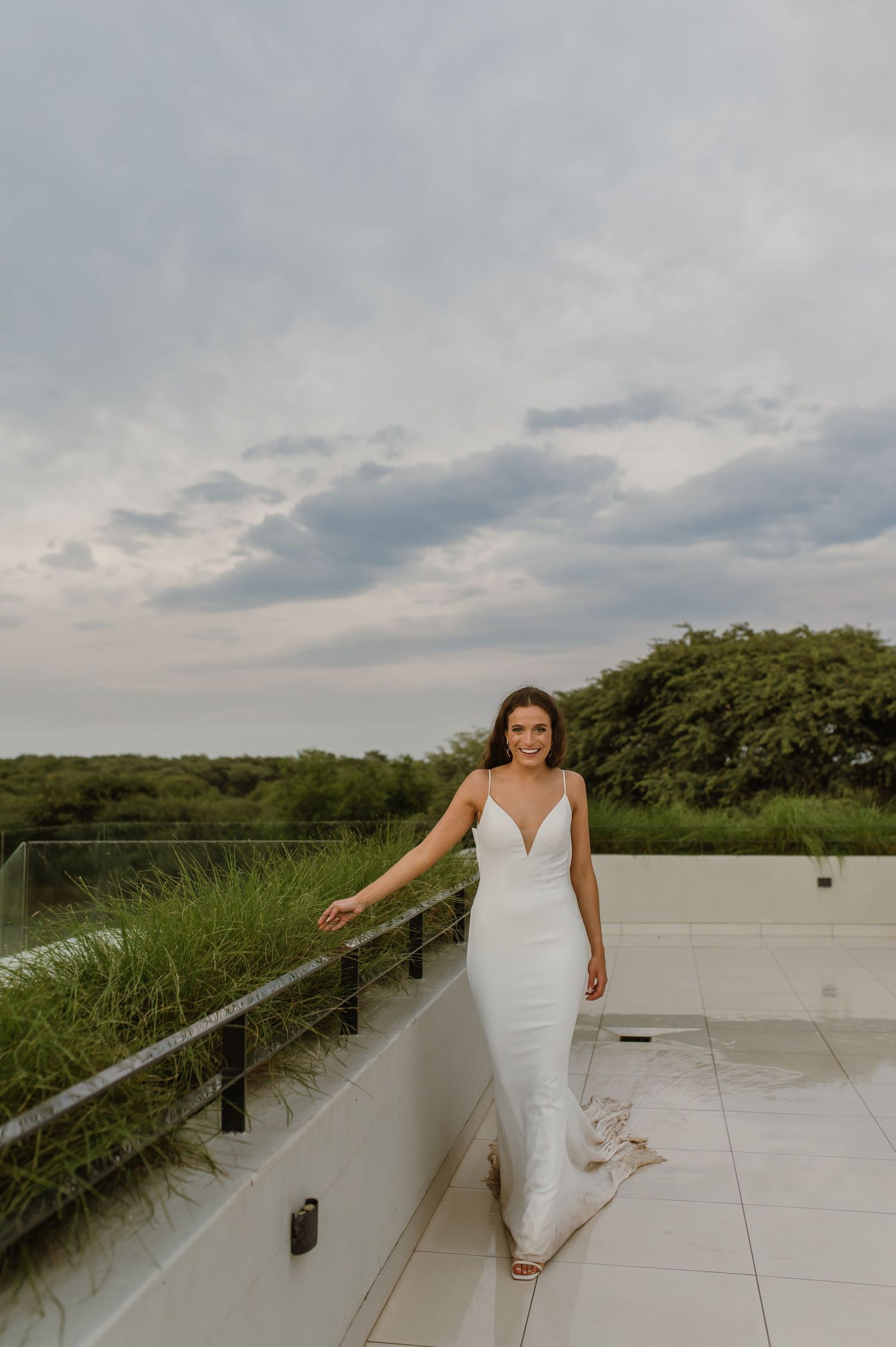 Bride in elegant fitted white dress poses on modern outdoor terrace.