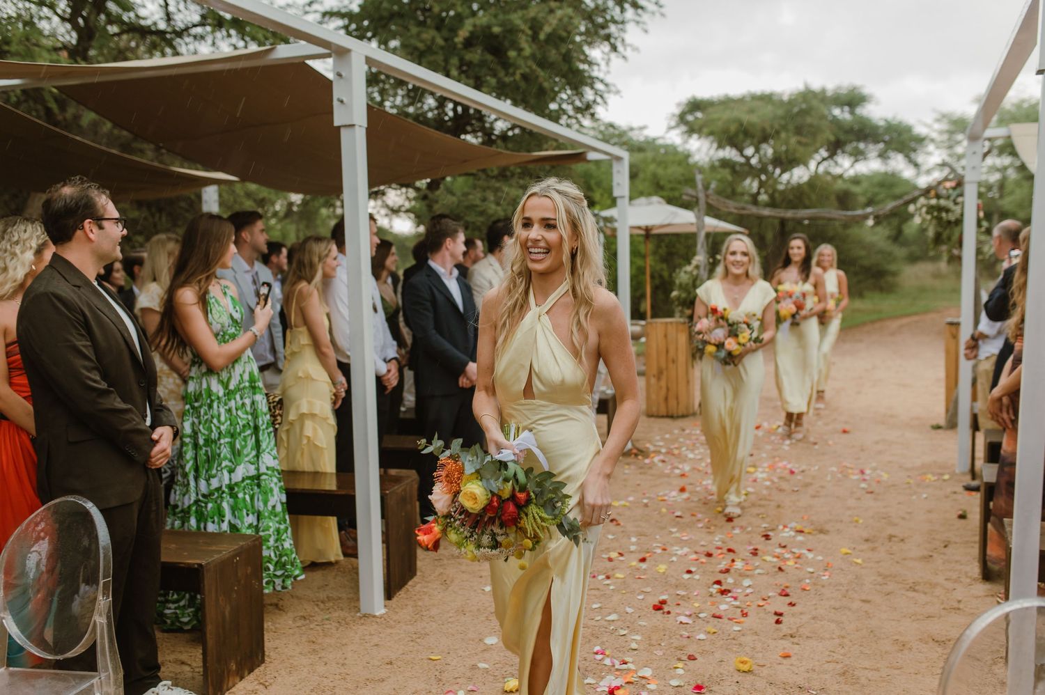 Wedding ceremony guests gather along a rose petal-lined aisle in a desert setting.