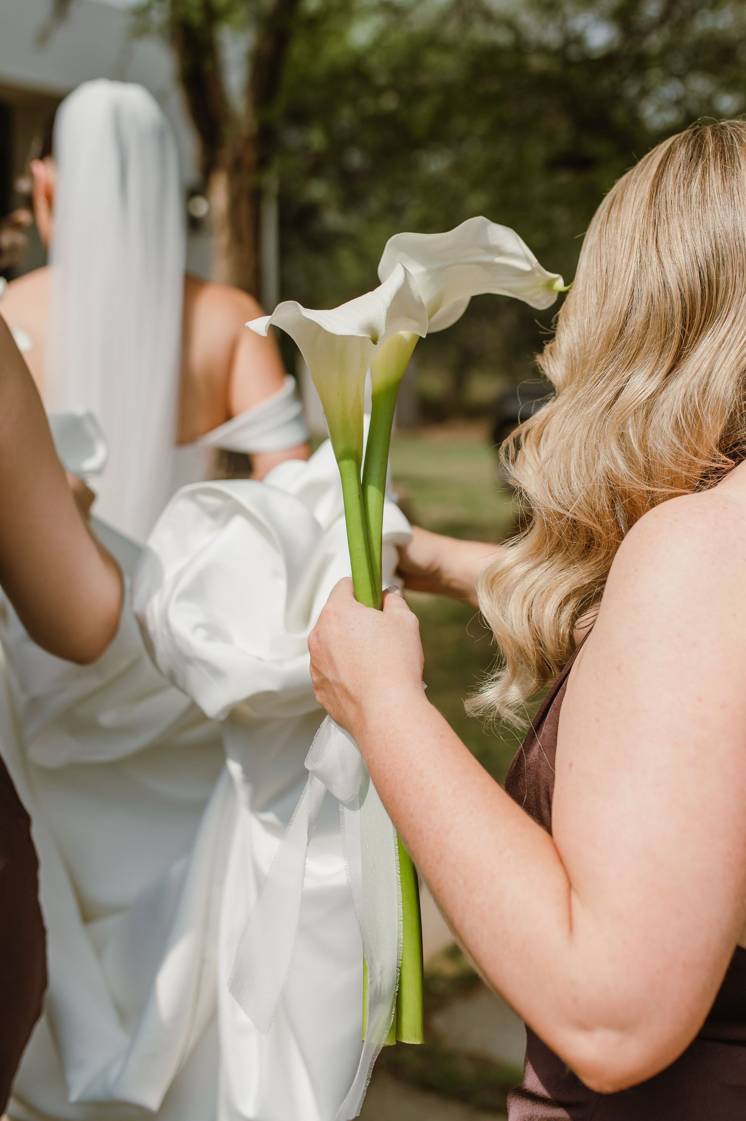 Wedding party members in white dresses holding bouquets against a natural outdoor backdrop.