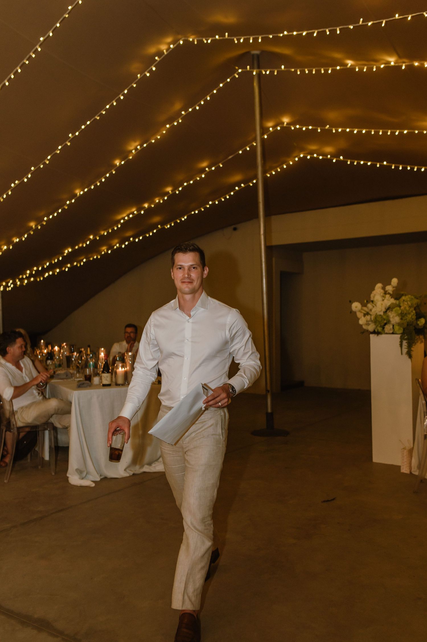Reception venue with string lights and elegant white table settings under a tent.