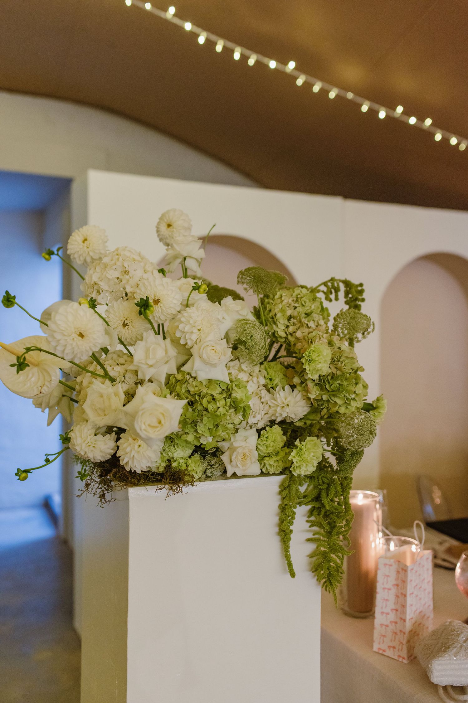 Elegant white floral arrangements with roses and greenery decorate a wedding reception table.