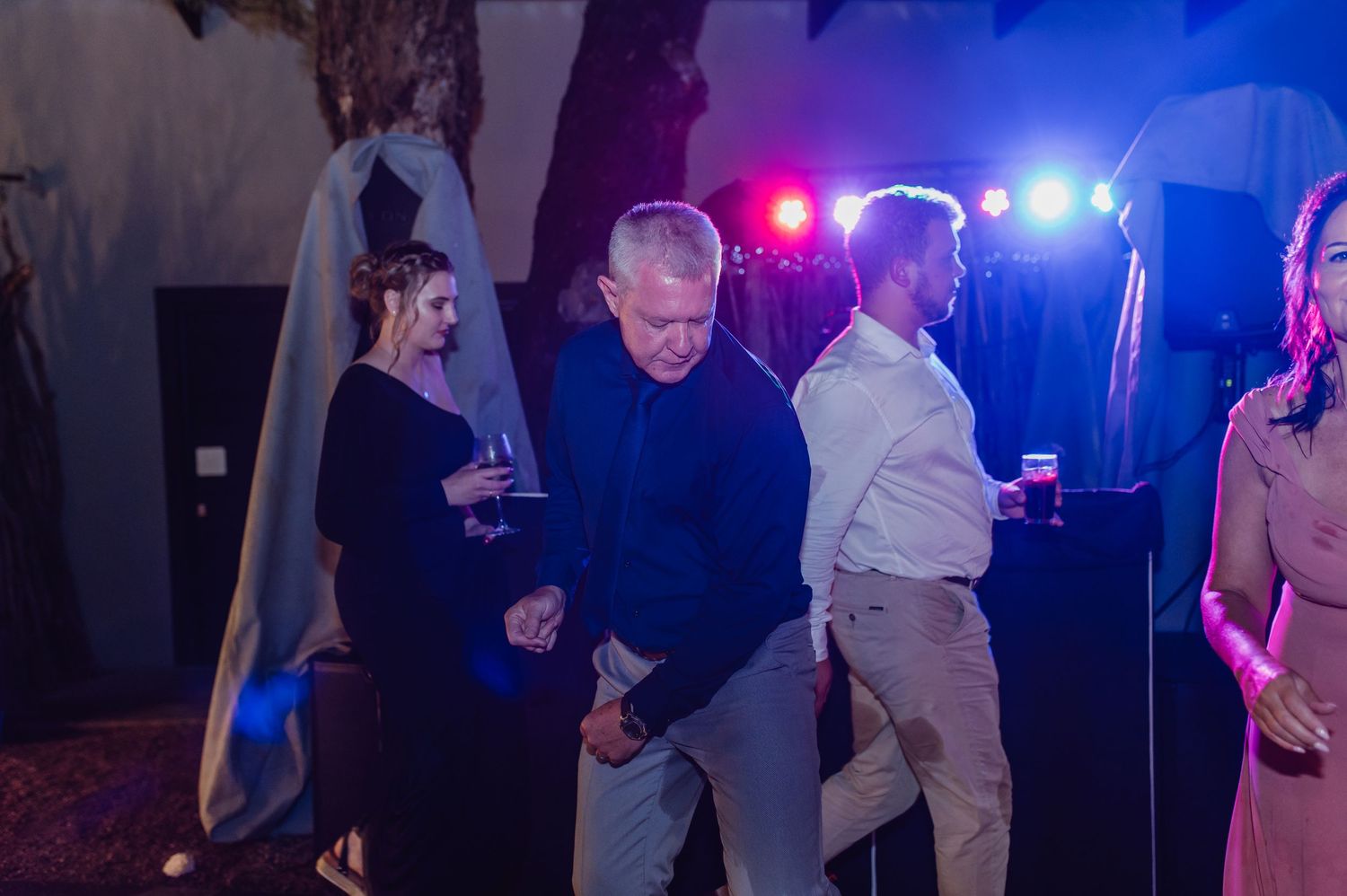 Wedding guests dancing under purple and blue disco lights at lively indoor evening reception.