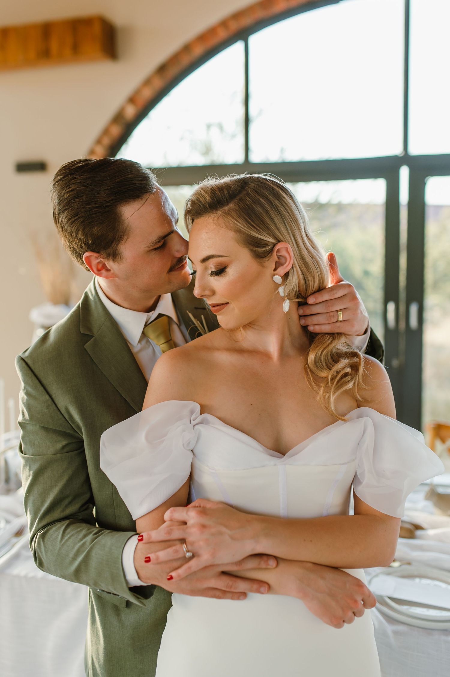 Intimate wedding portrait in front of arched windows with natural lighting.