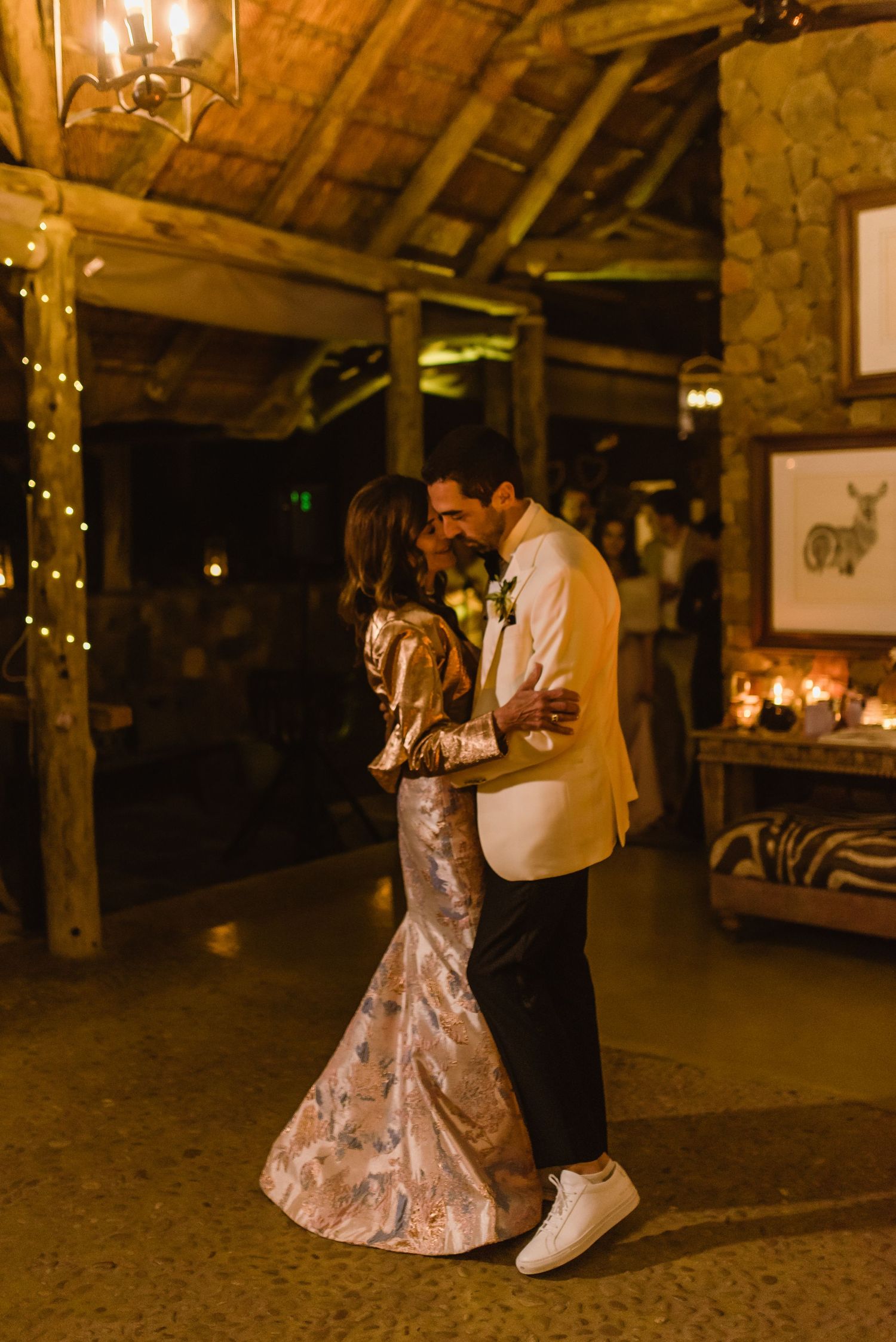 Couples enjoying first dances in warmly lit rustic barn reception space.