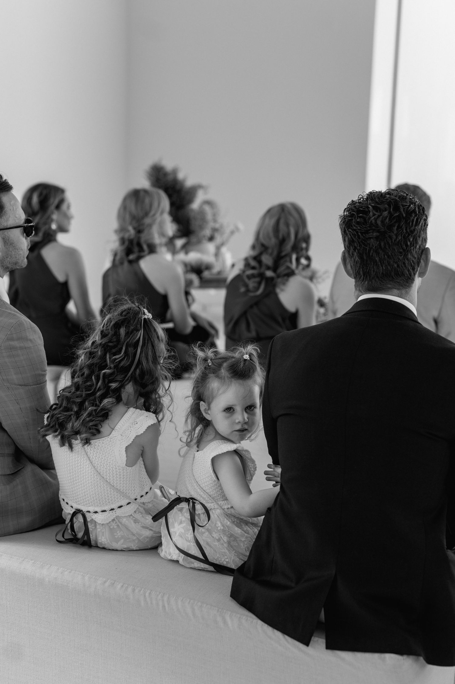 Black and white photo of wedding guests seated on floor during ceremony.