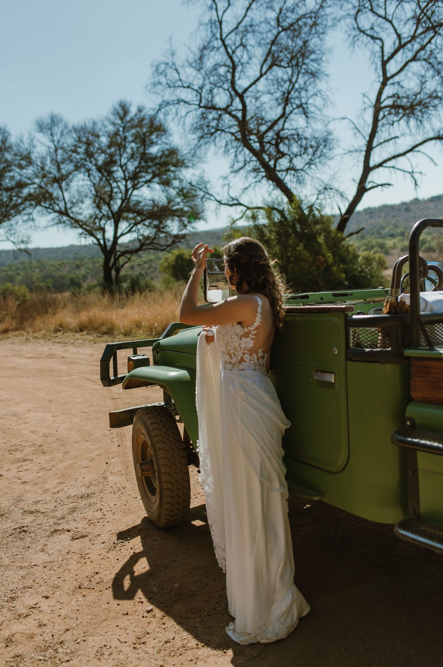 Bride leans against classic green car during desert wedding photoshoot.