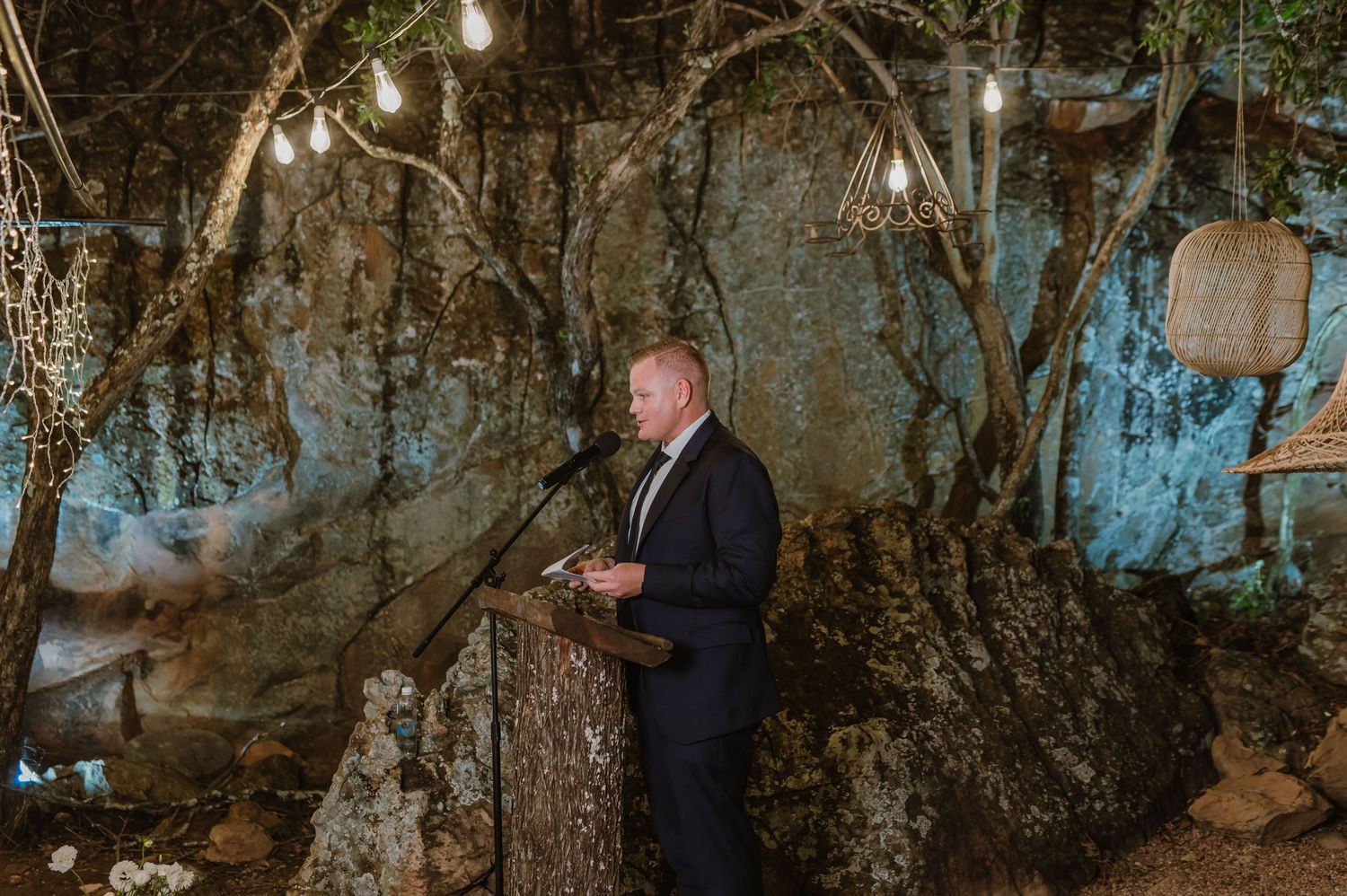 Outdoor evening wedding ceremony space with natural tree backdrop and soft lighting.