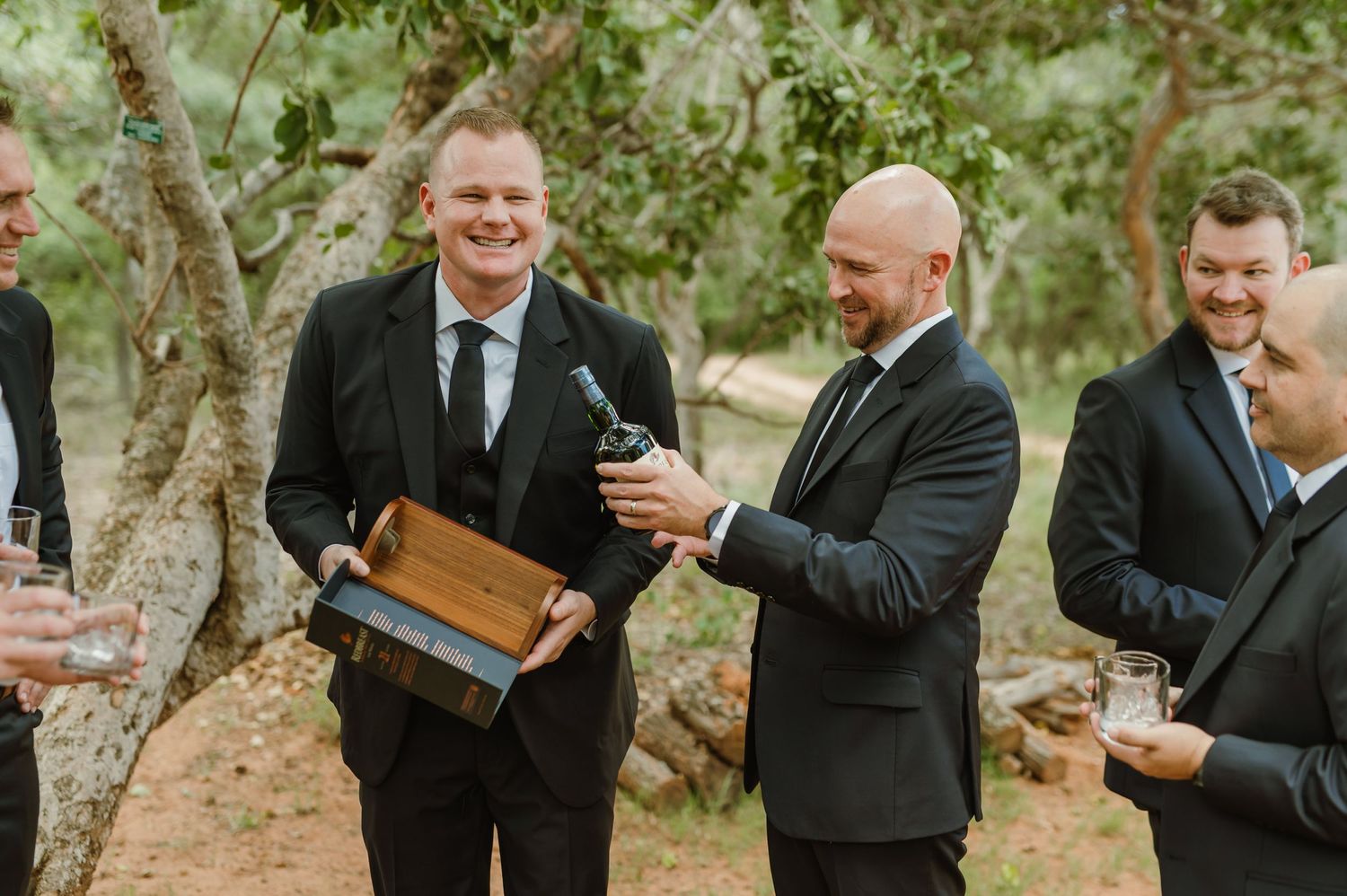 Group of men in suits sharing a celebratory moment with books outdoors.
