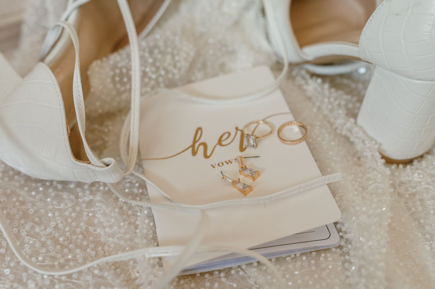 Wedding accessories including white shoes and 'her' labeled items arranged on sparkly surface.