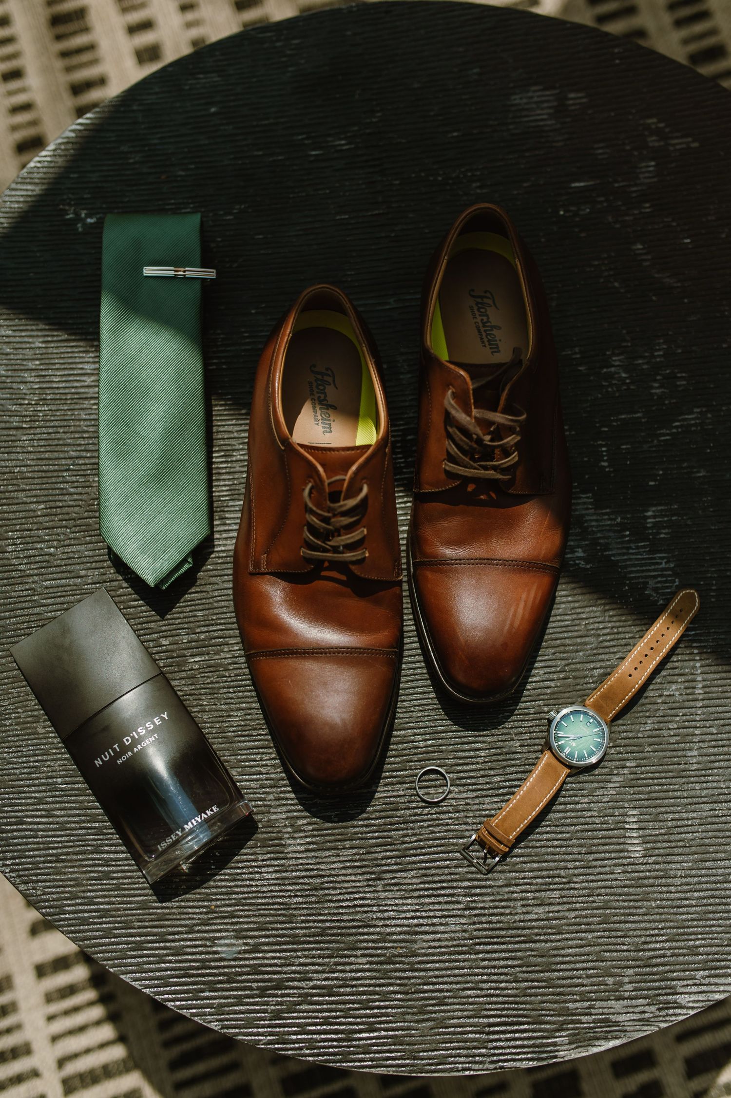 Brown leather dress shoes and green ties arranged on a dark surface.