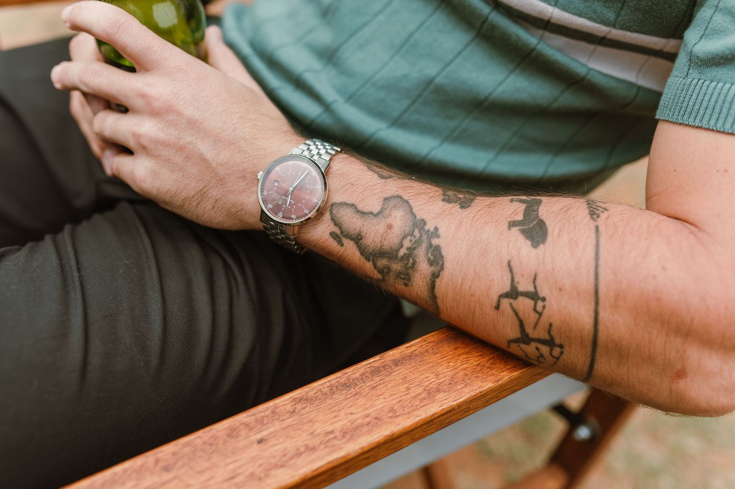 Tattooed arm resting on wooden surface showing intricate designs.