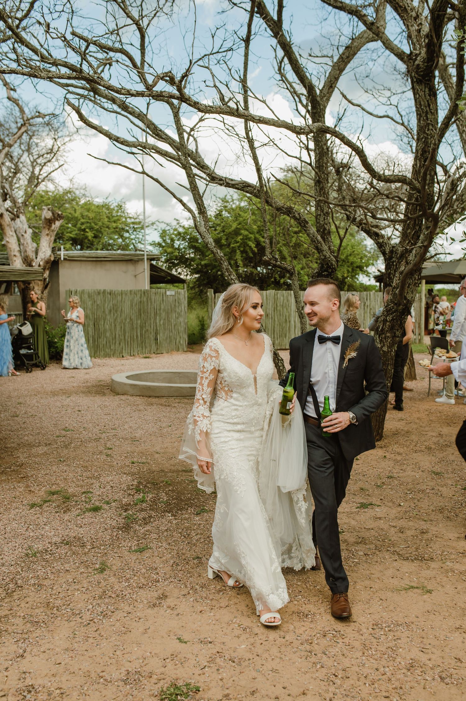 Wedding couple walking together on a dirt path surrounded by trees and natural scenery.