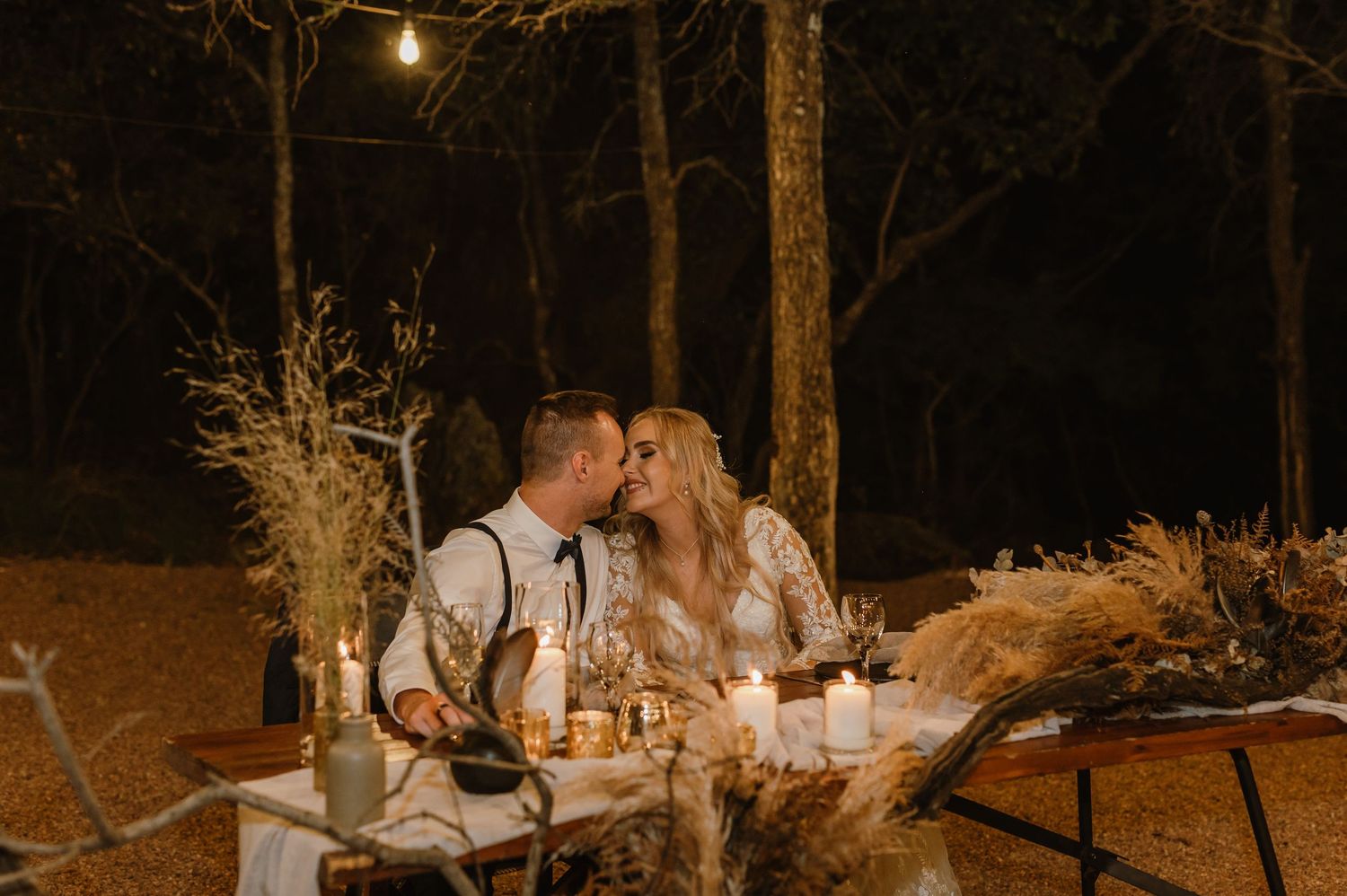 A romantic candlelit sweetheart table decorated with pampas grass at an outdoor wedding.