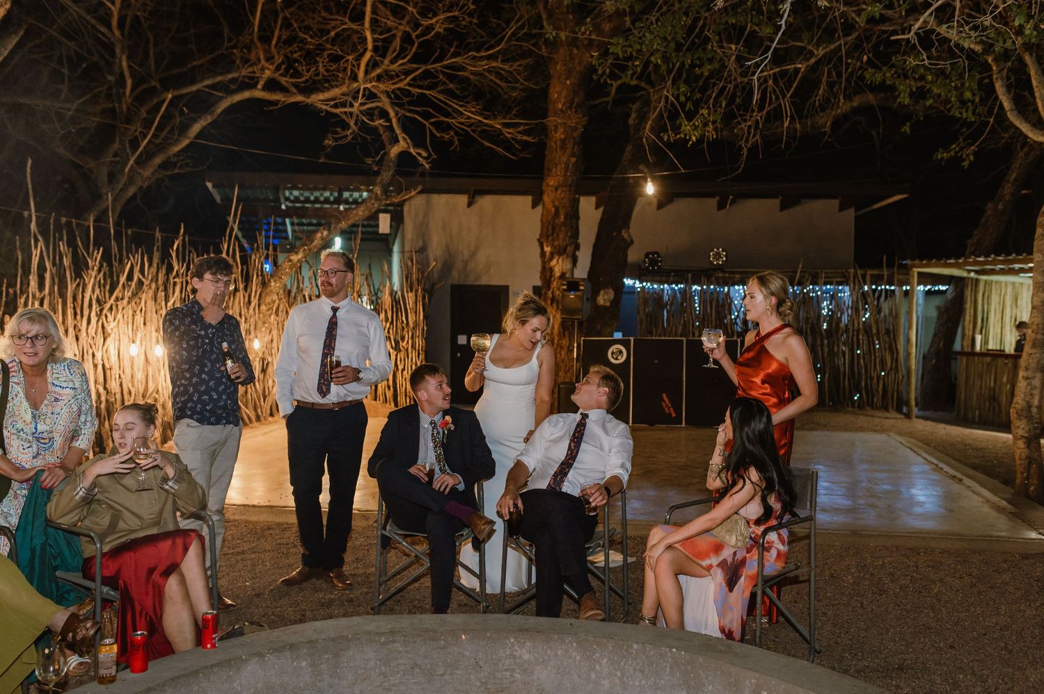 Outdoor wedding reception with guests dancing under string lights at night.
