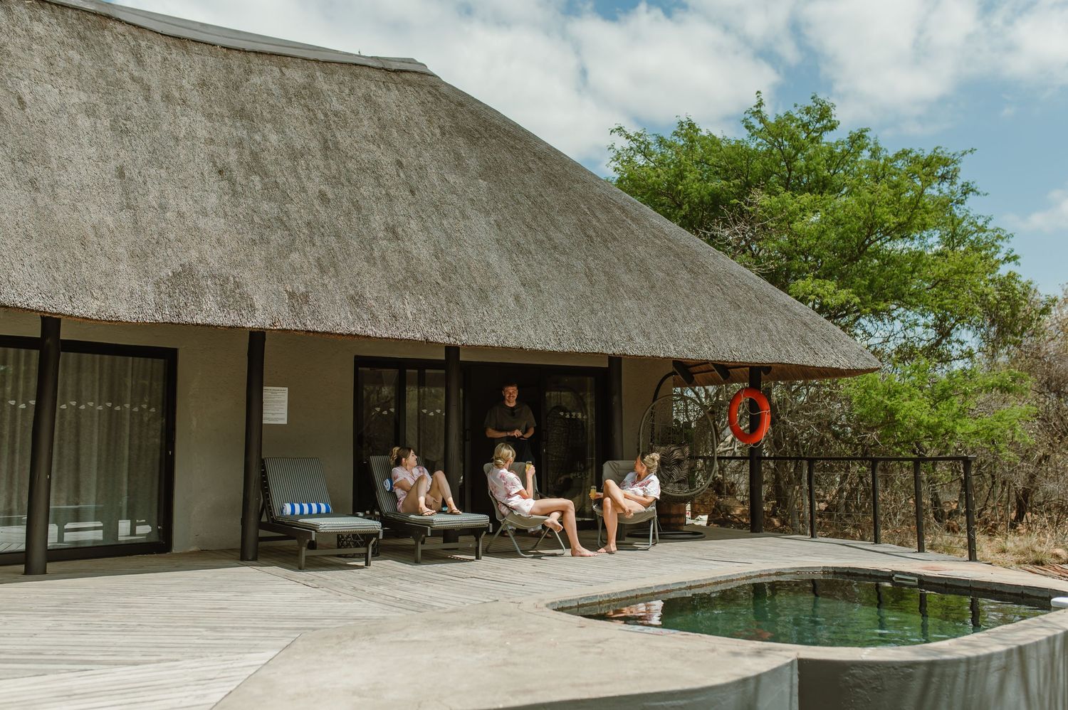 Rustic thatched-roof lodge buildings with outdoor seating areas in a natural setting.