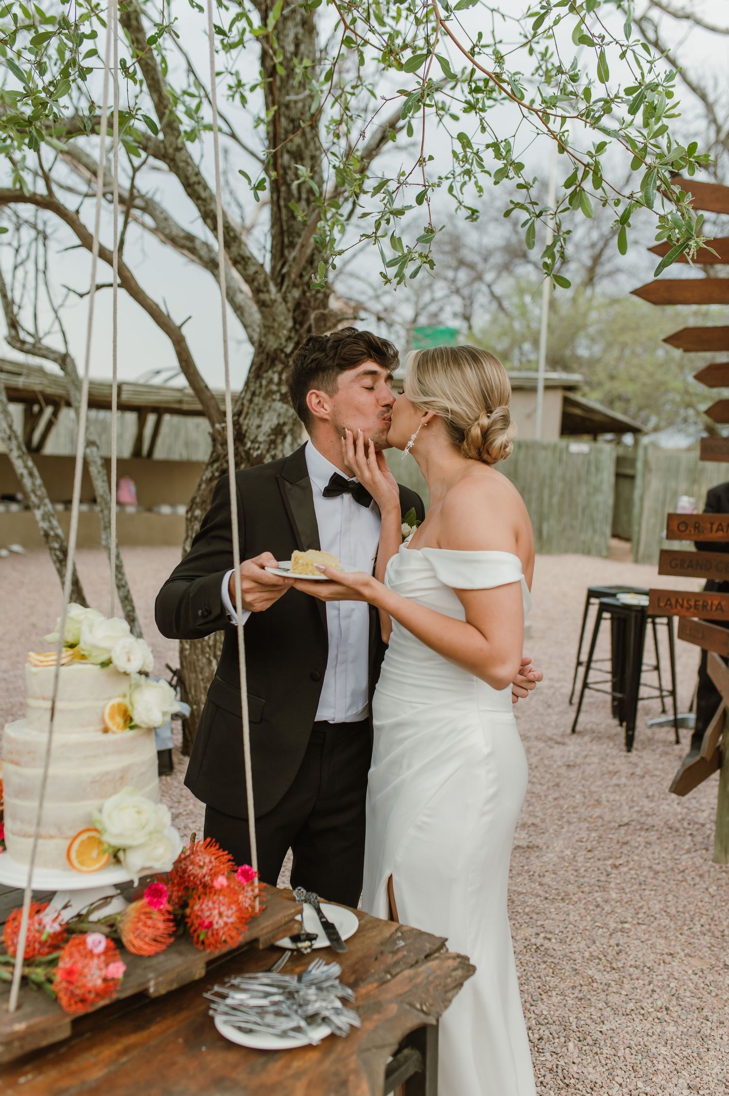 Newlyweds enjoying their wedding cake together on a wooden swing in a garden setting.