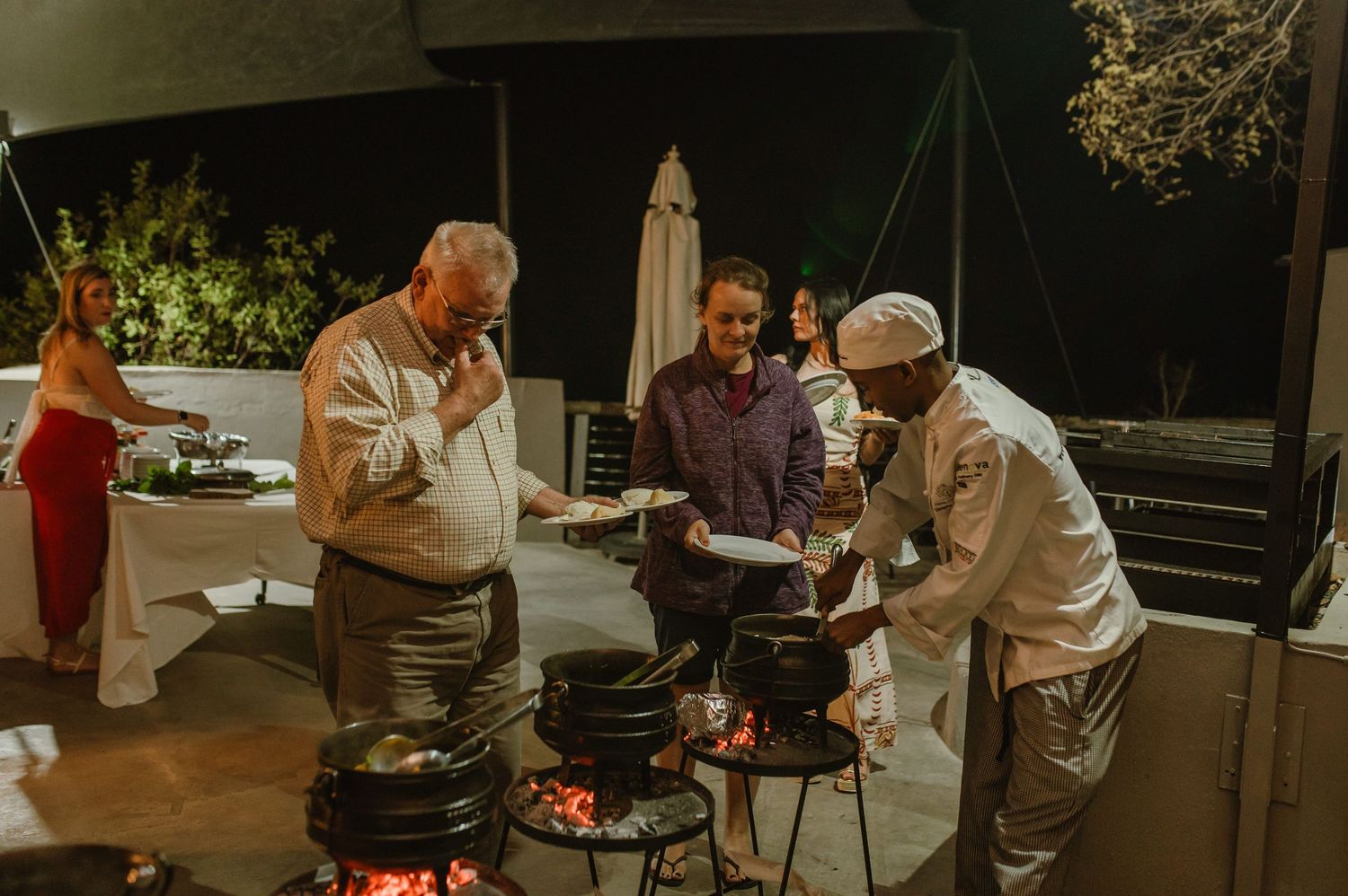Chefs gathered around outdoor grills preparing food at night.