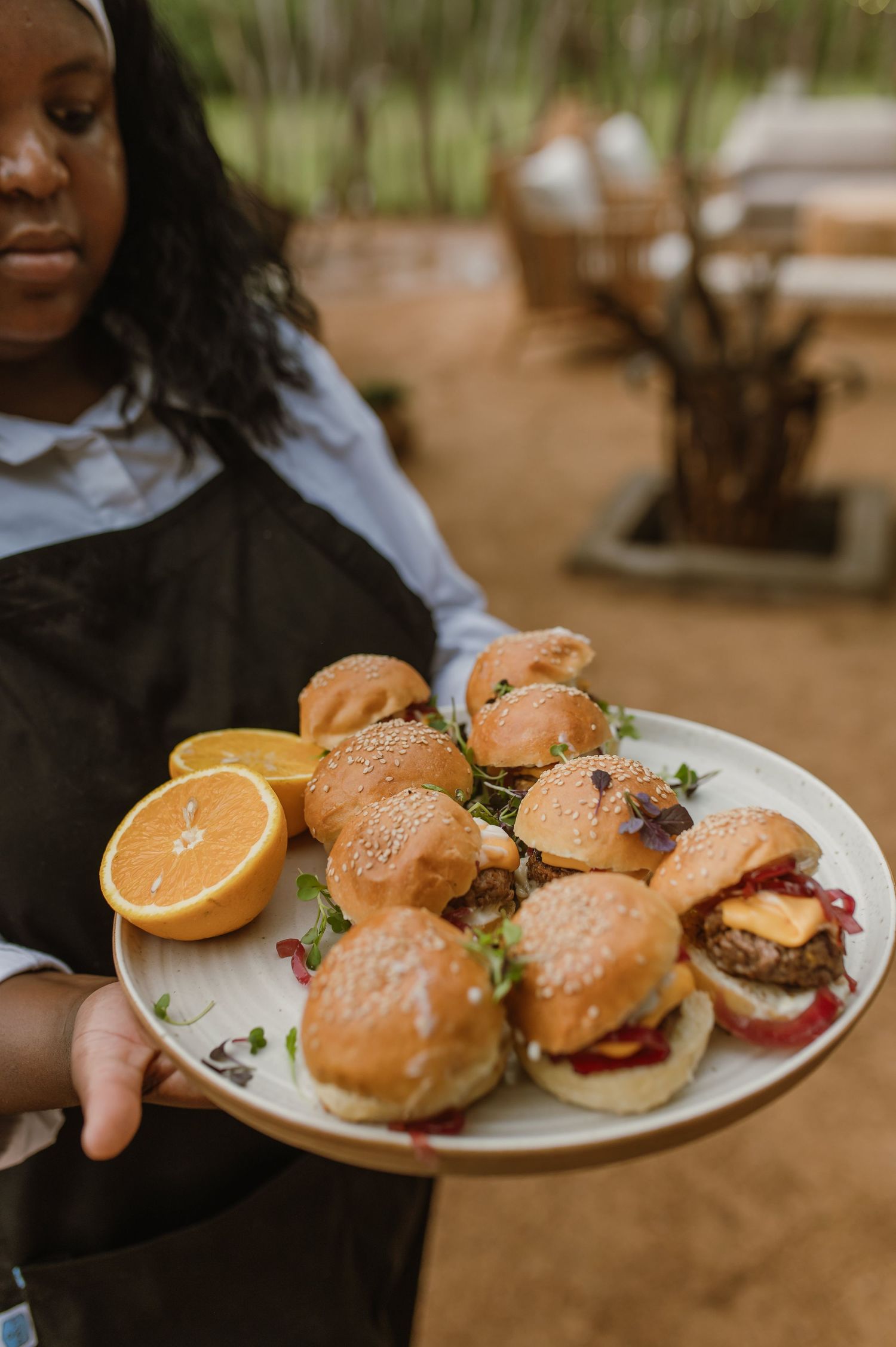 Plate of mini sliders with orange slices being served at an outdoor event.
