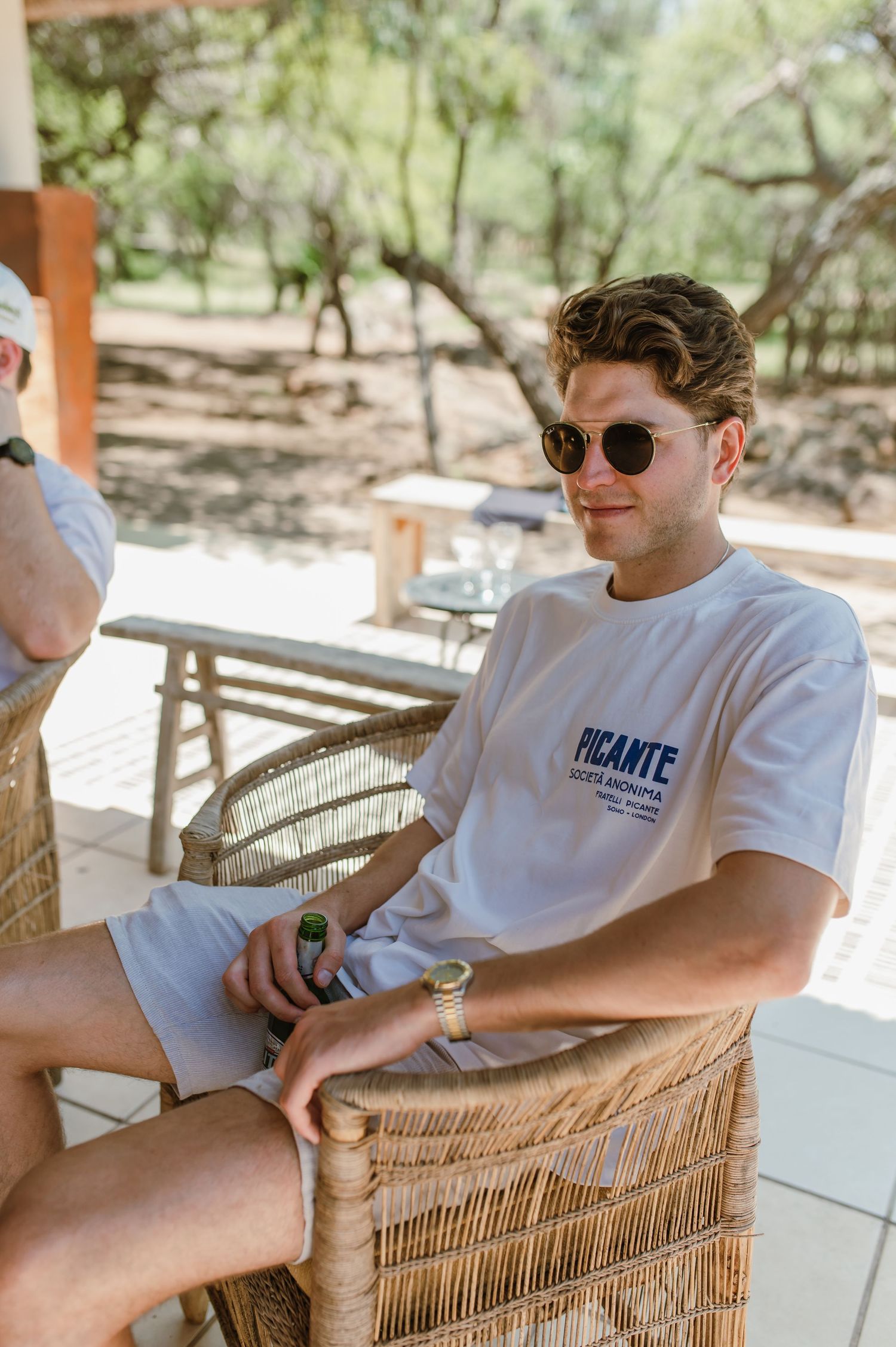 Person relaxing in wicker chair on outdoor patio wearing sunglasses.