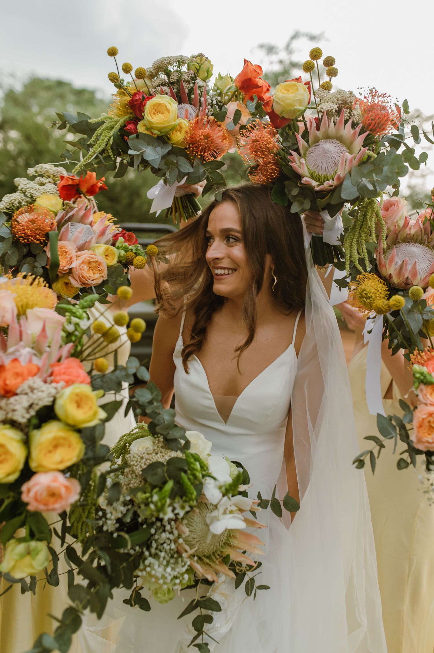 Beautiful floral arch with protea and roses frames outdoor bridal portrait.