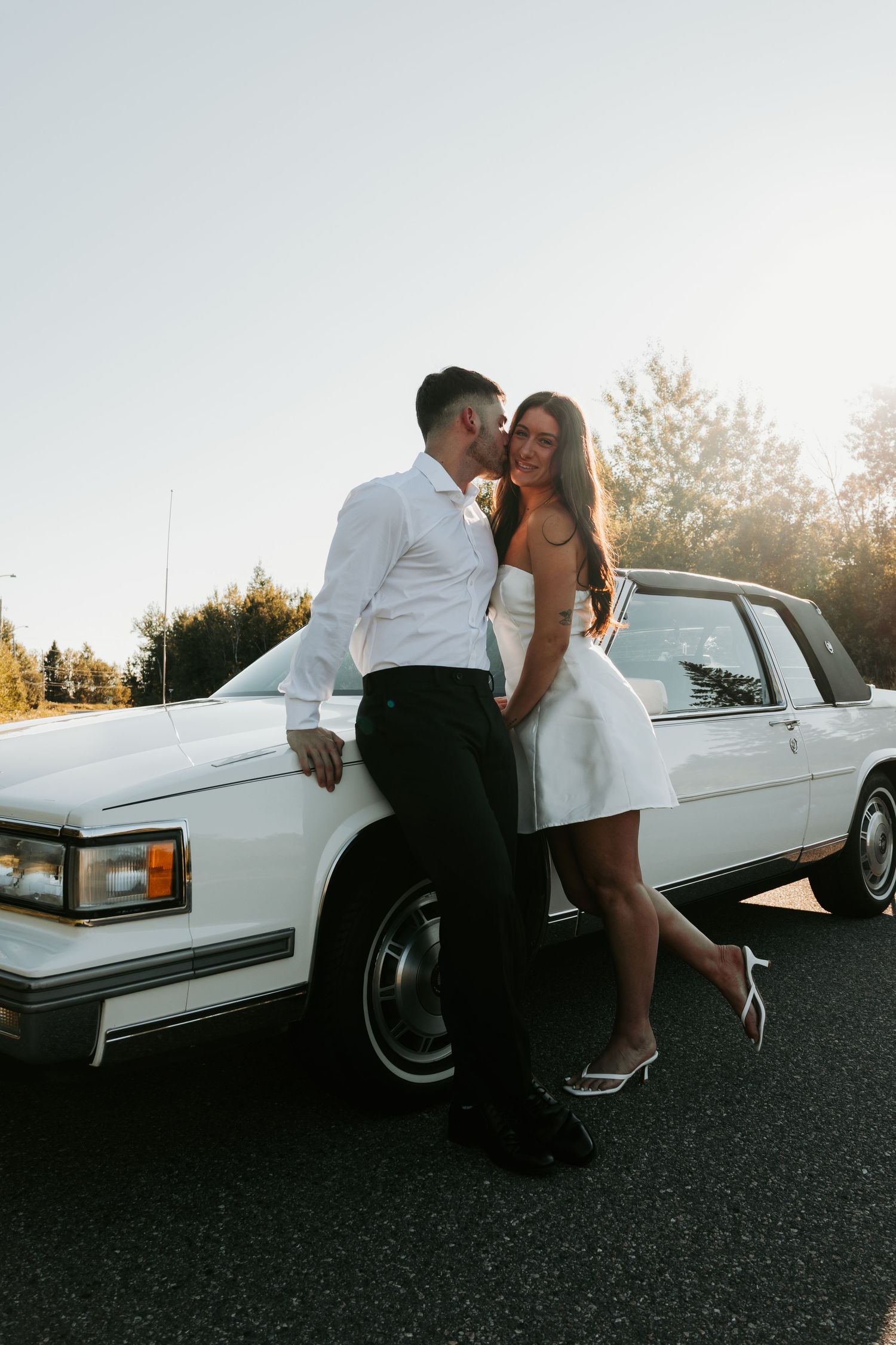 Couple embraces by classic white Cadillac during golden hour photo session.