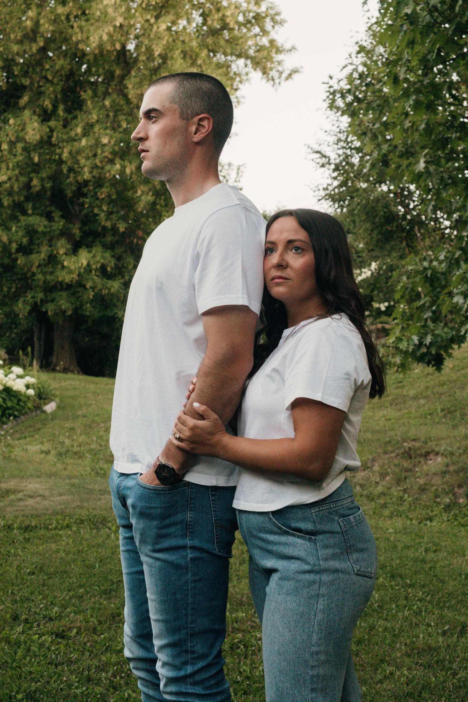 Couple in casual white shirts and jeans embracing outdoors against a green backdrop.