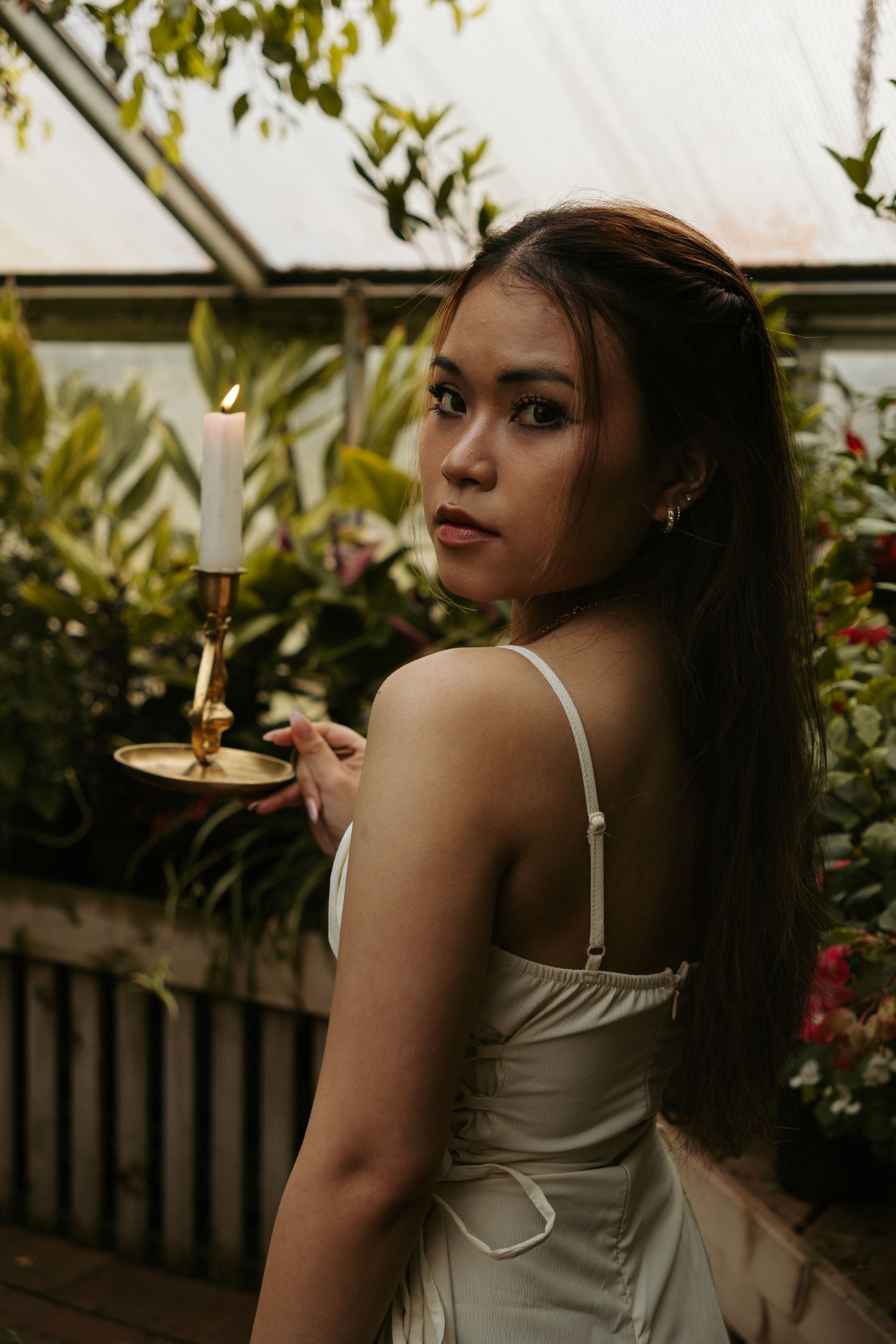 Woman in white dress poses against lush garden backdrop.