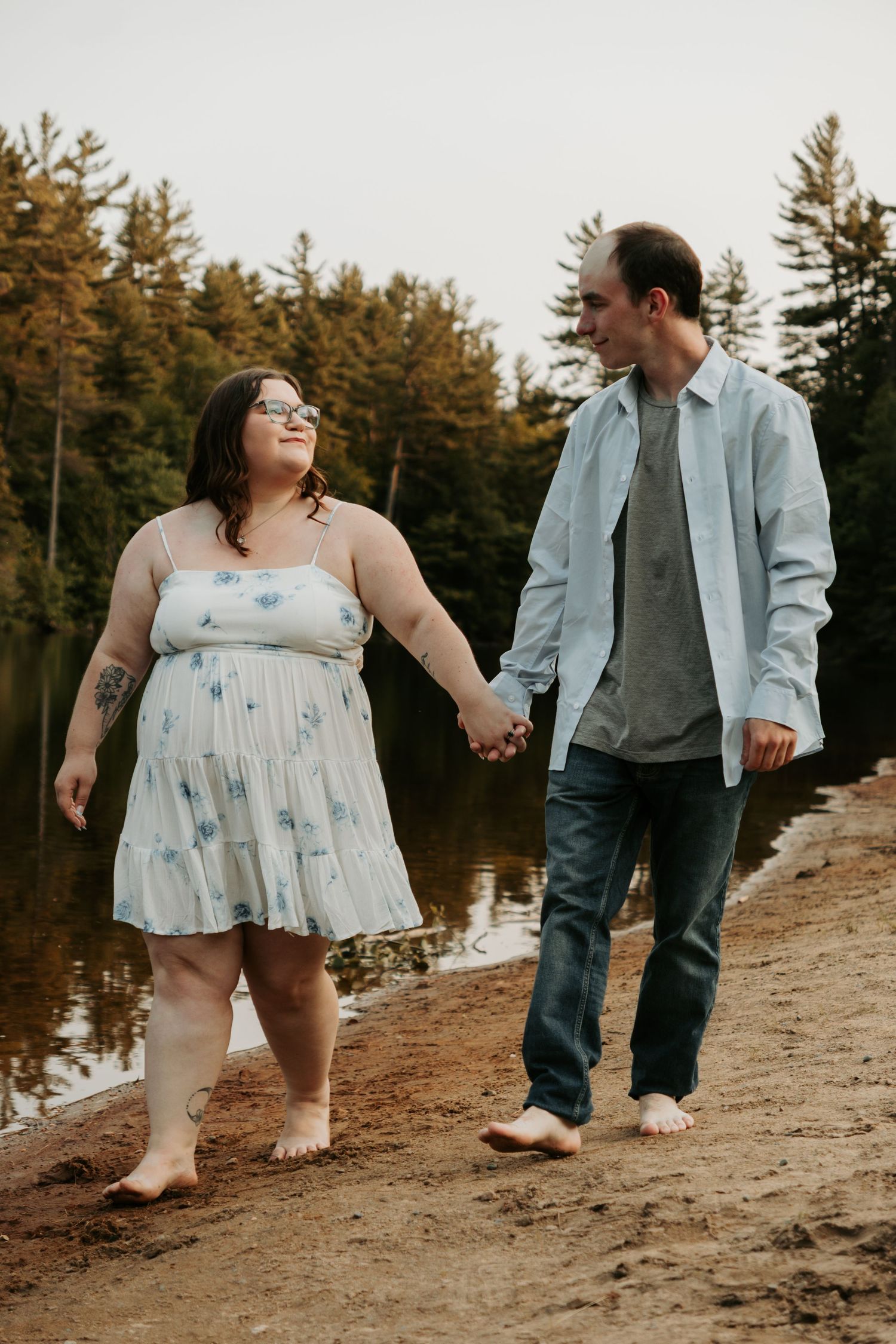 Couple walks barefoot along sandy beach near water's edge.