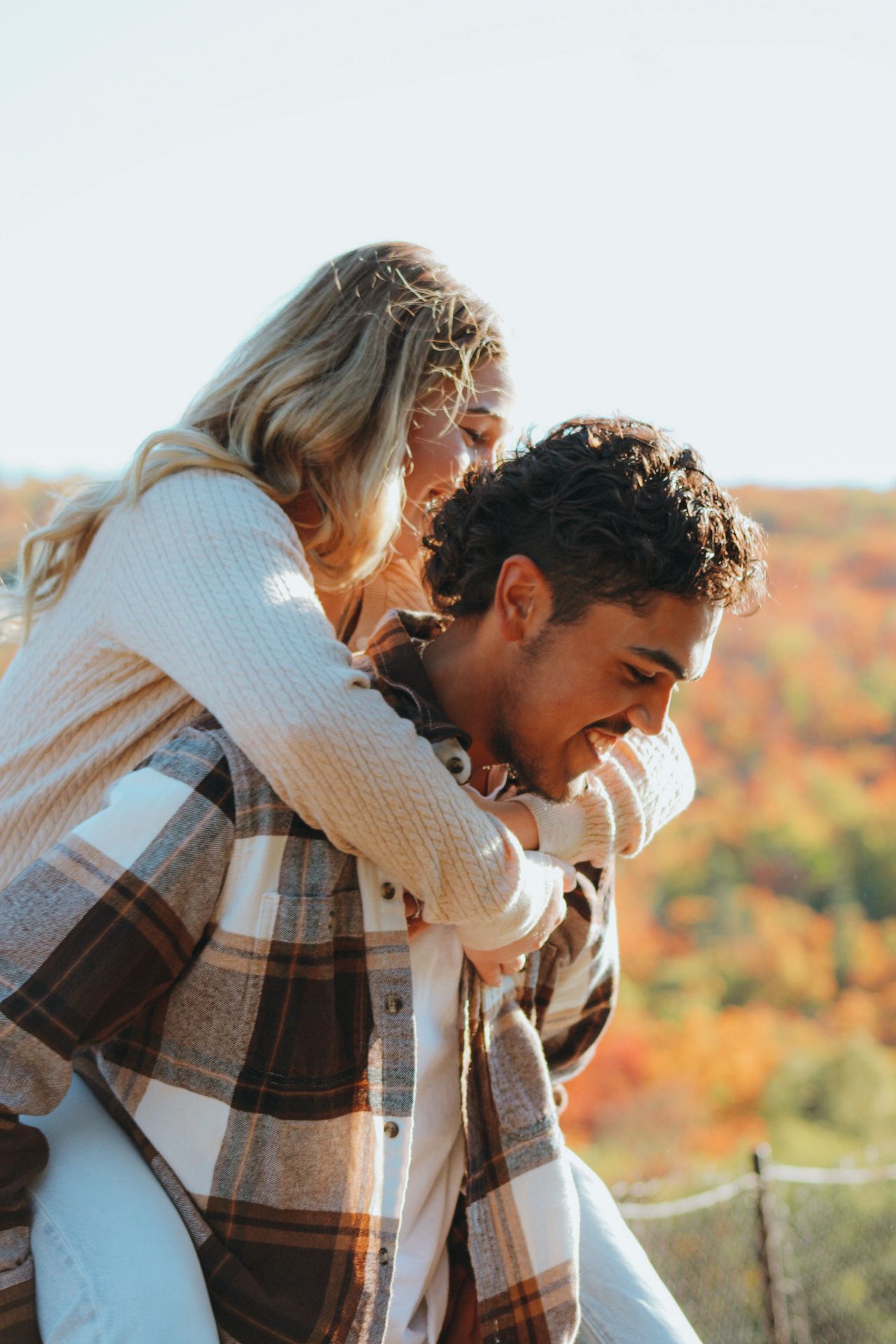 Couple sharing intimate moment wearing plaid flannel against fall foliage backdrop.